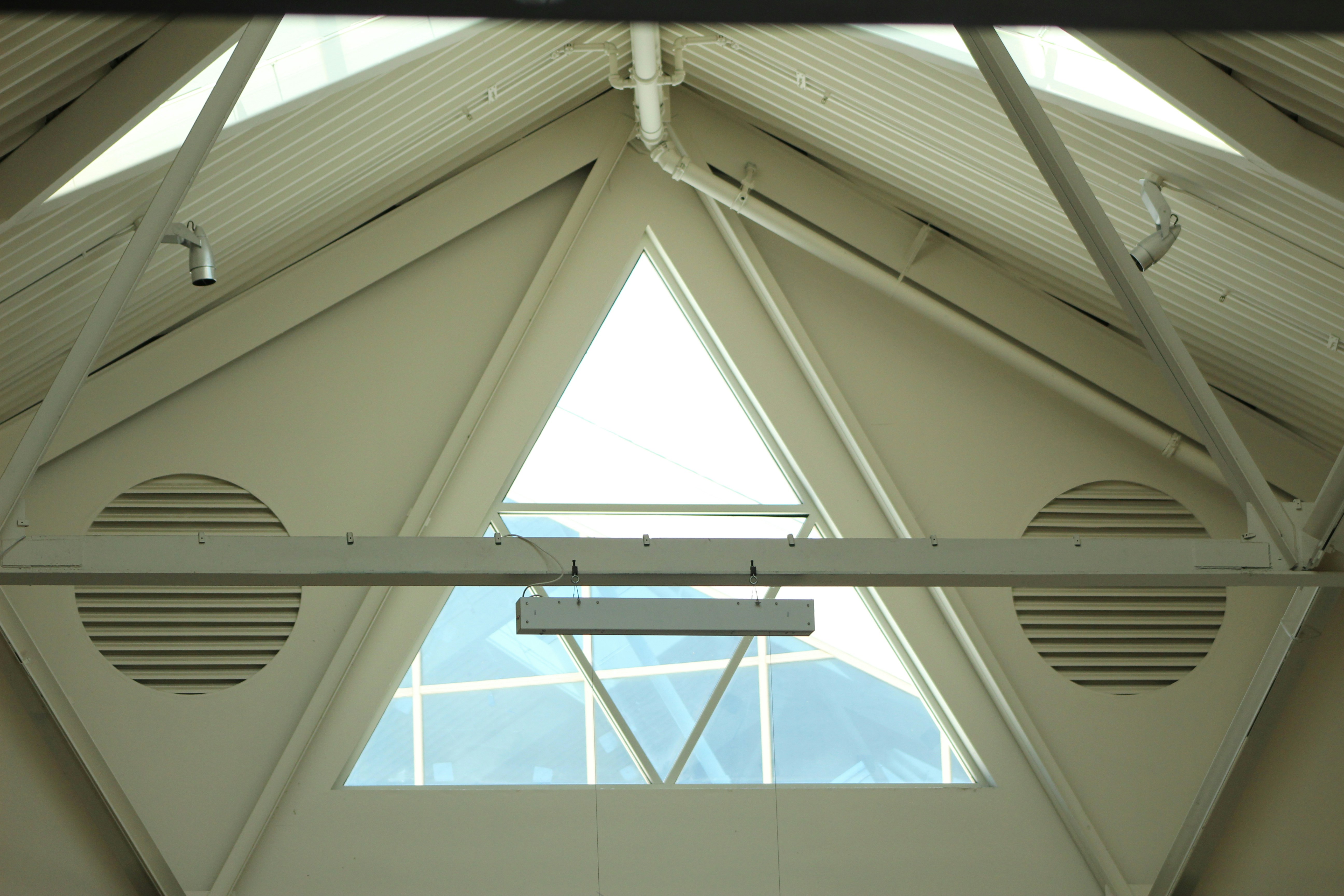 A triangular window in a white metal ceiling with circular ventilation grilles