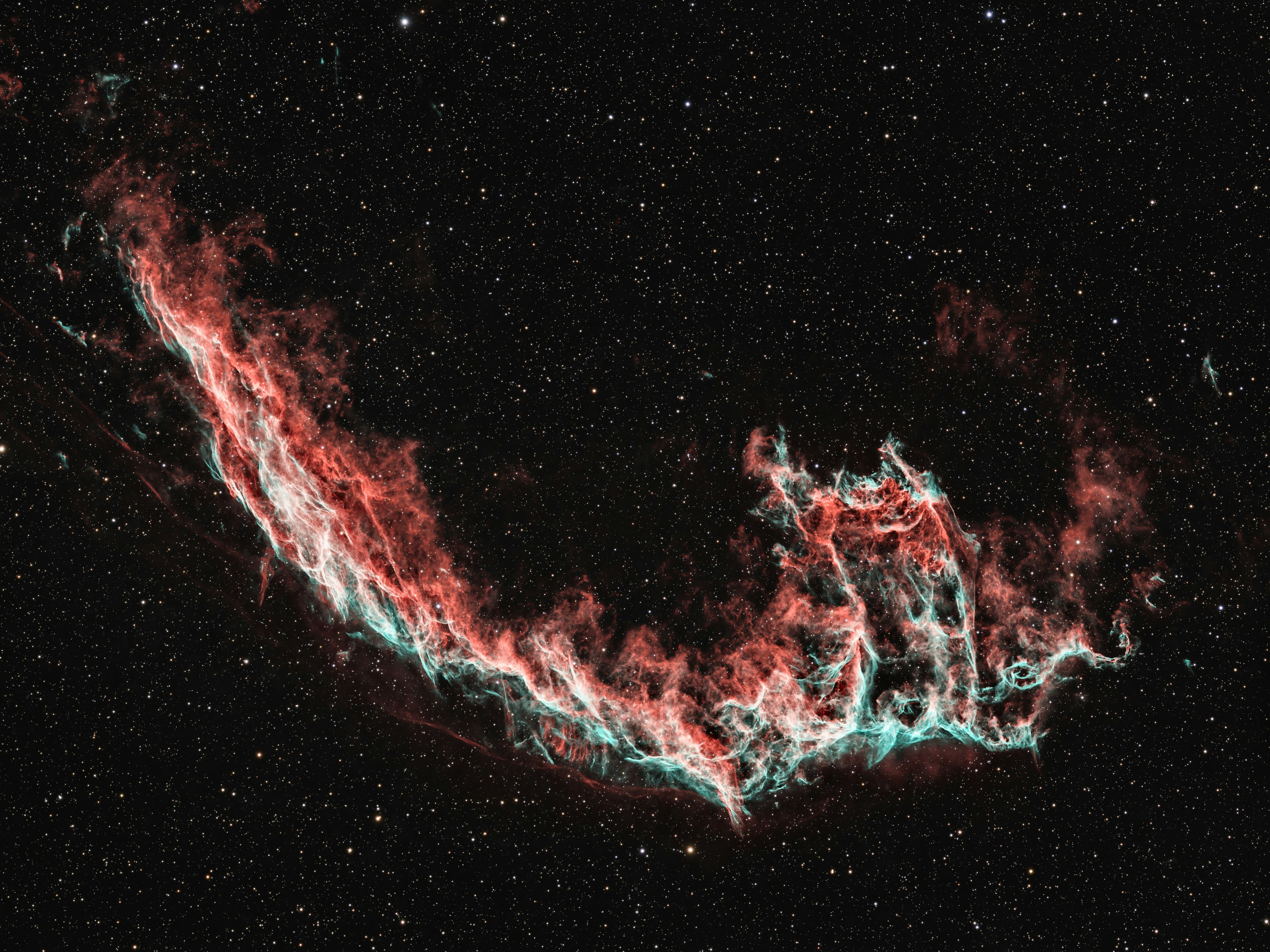 La Nebulosa del Velo Oriental brillando en rojo y verde azulado contra un campo de estrellas