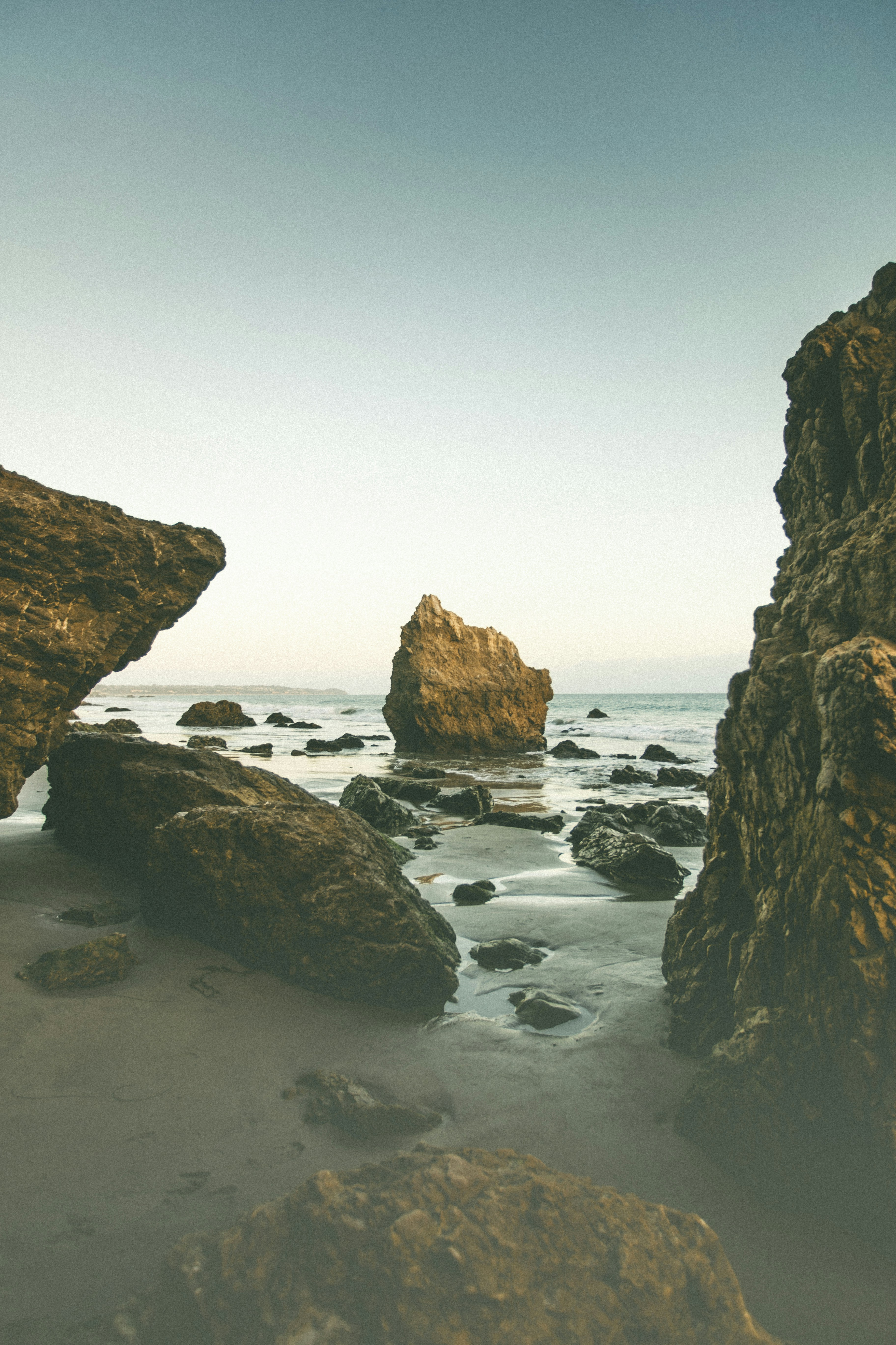 Large jagged rocks on a sandy beach with the ocean in the distance