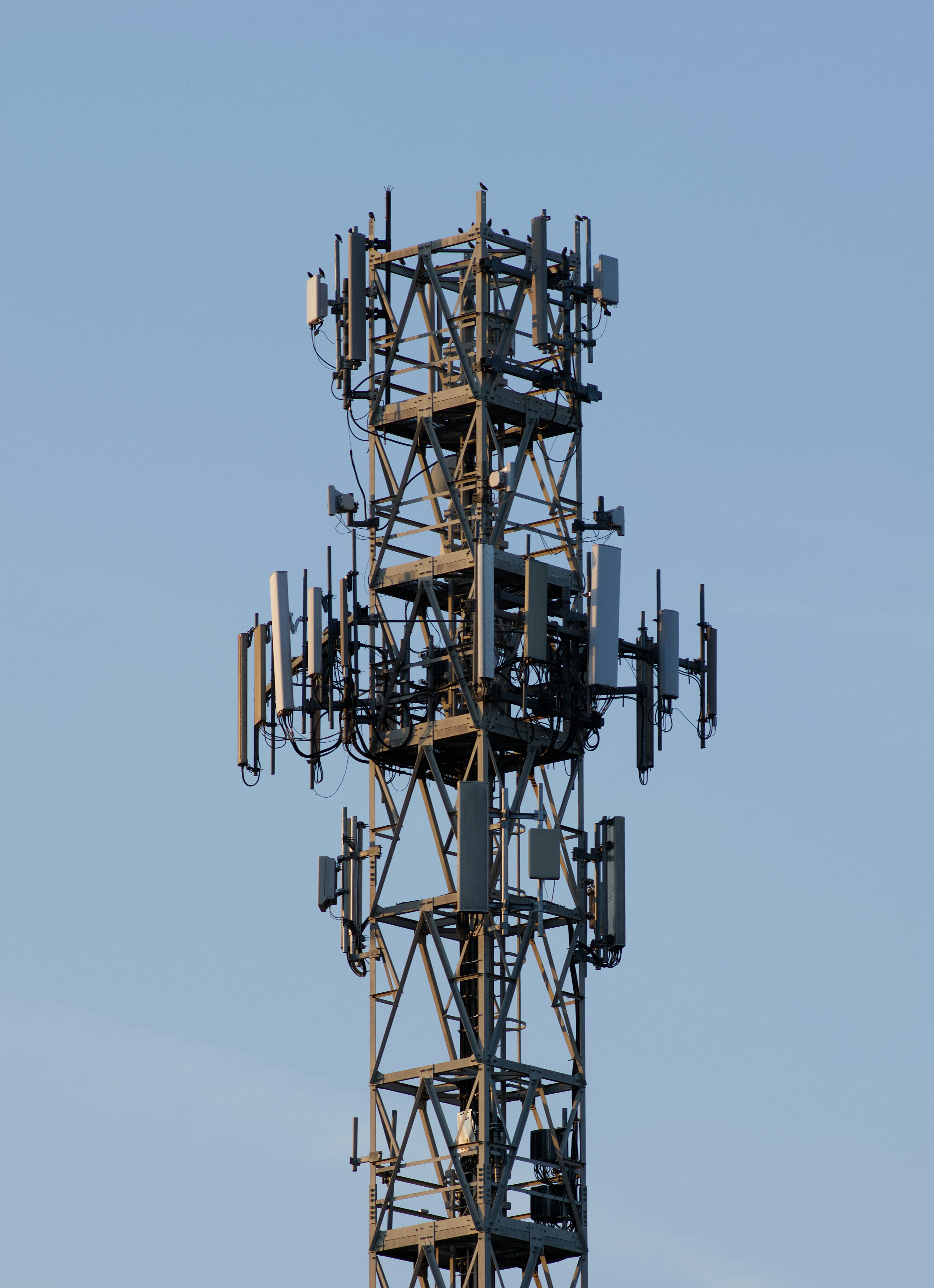 A tall metal cellular tower with multiple antennas against a clear blue sky