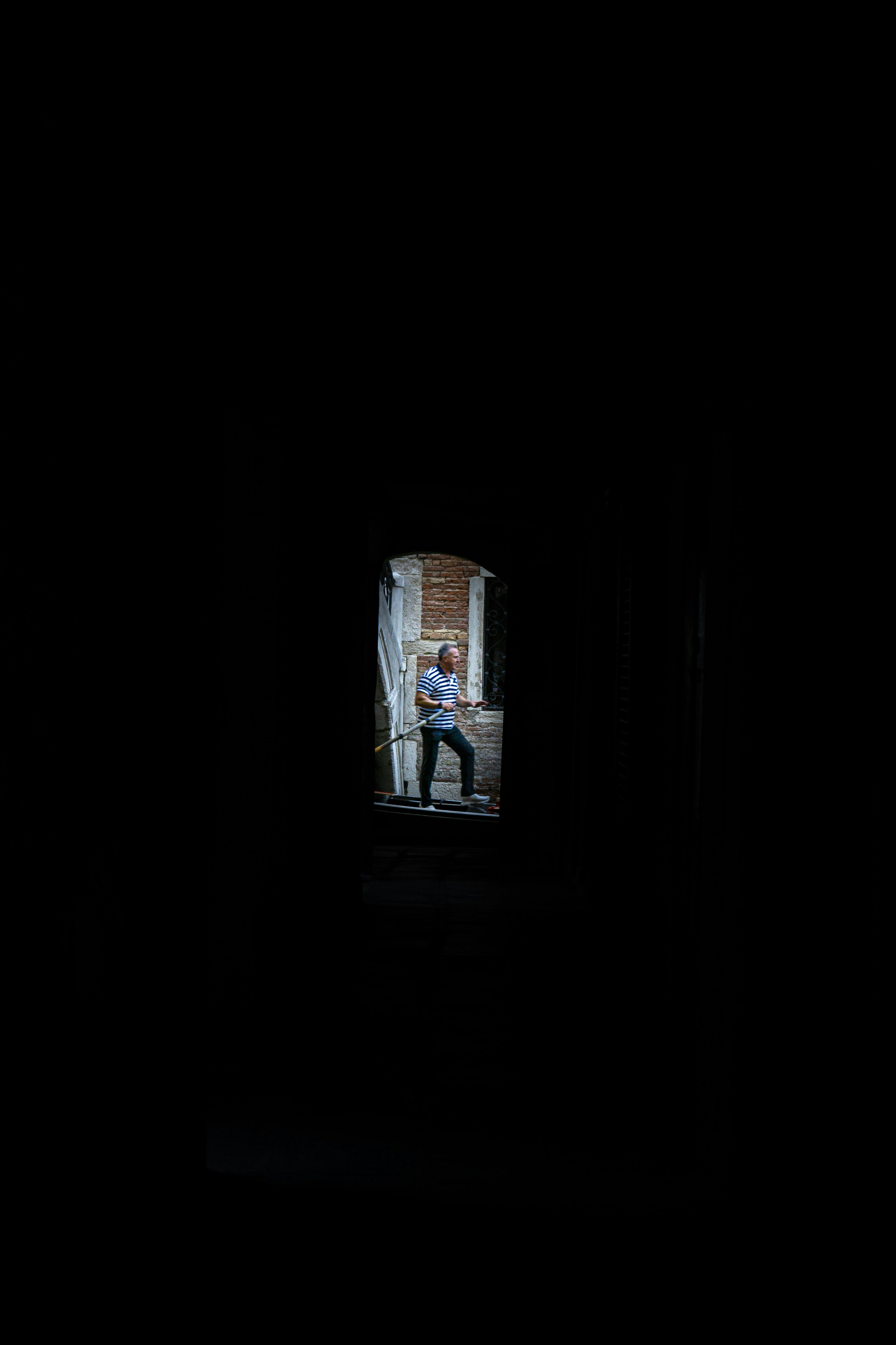 A man in a striped shirt rowing a boat through a dark stone archway
