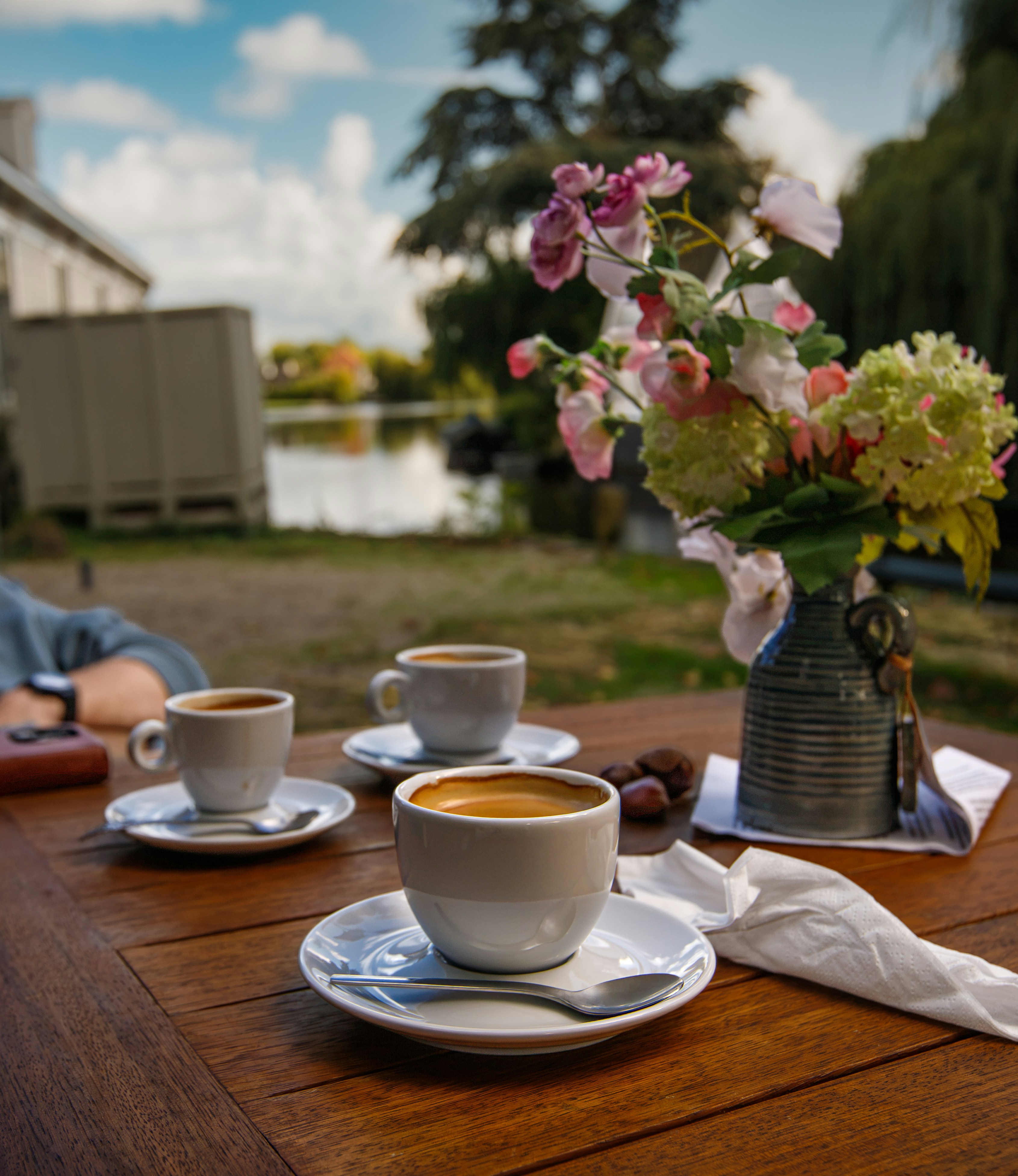 Three cups of coffee on a wooden table with a vase of flowers