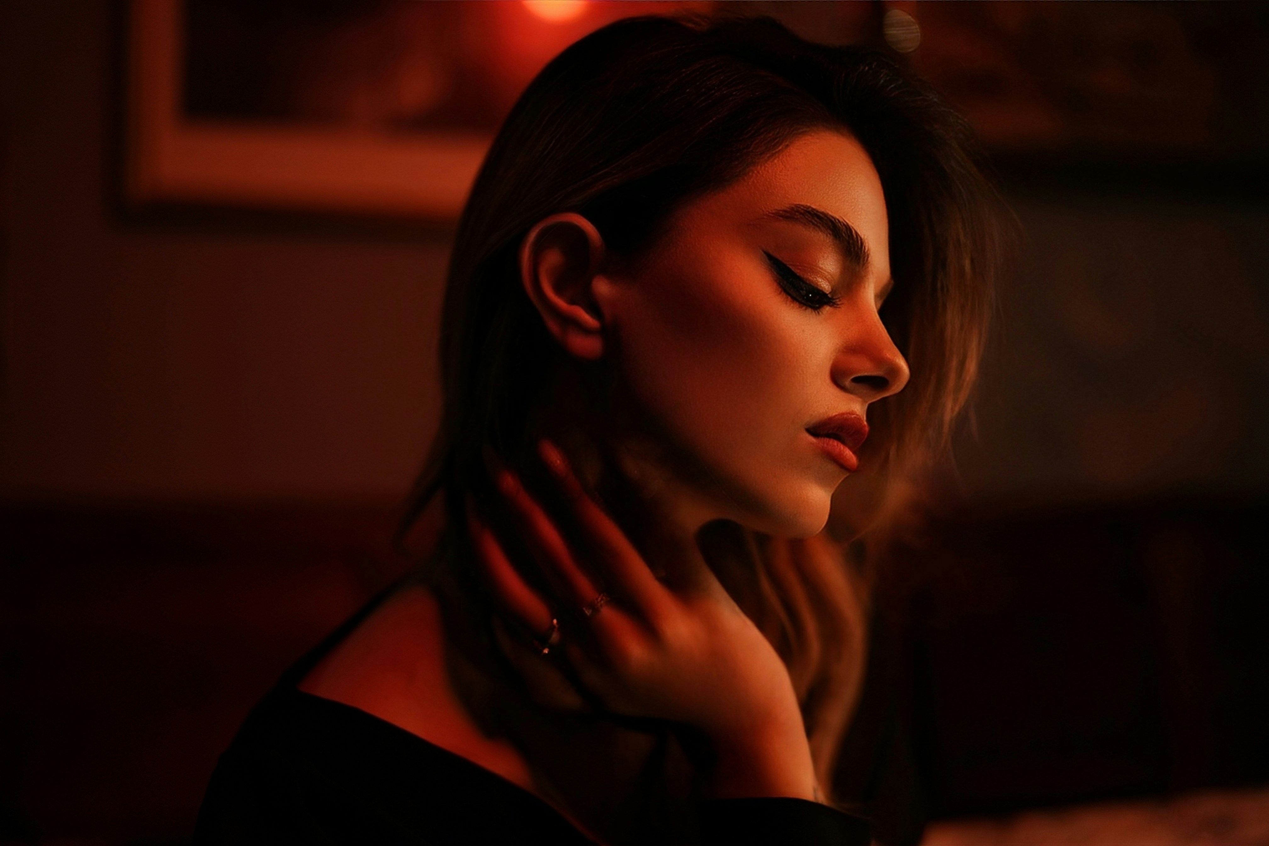 A woman in profile with her hand on her neck under warm red light