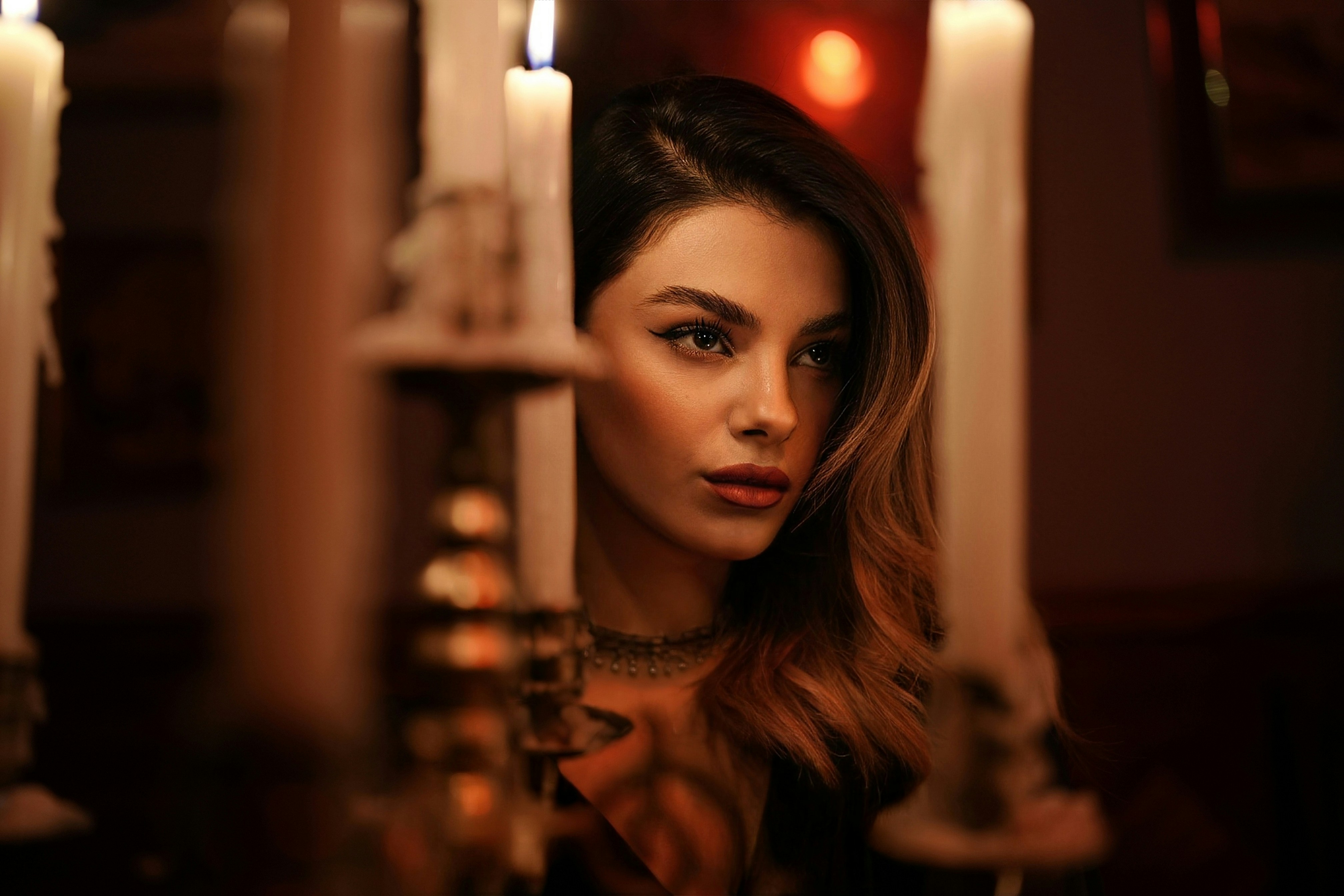 Una donna con capelli mossi dietro candele bianche in una stanza debolmente illuminata