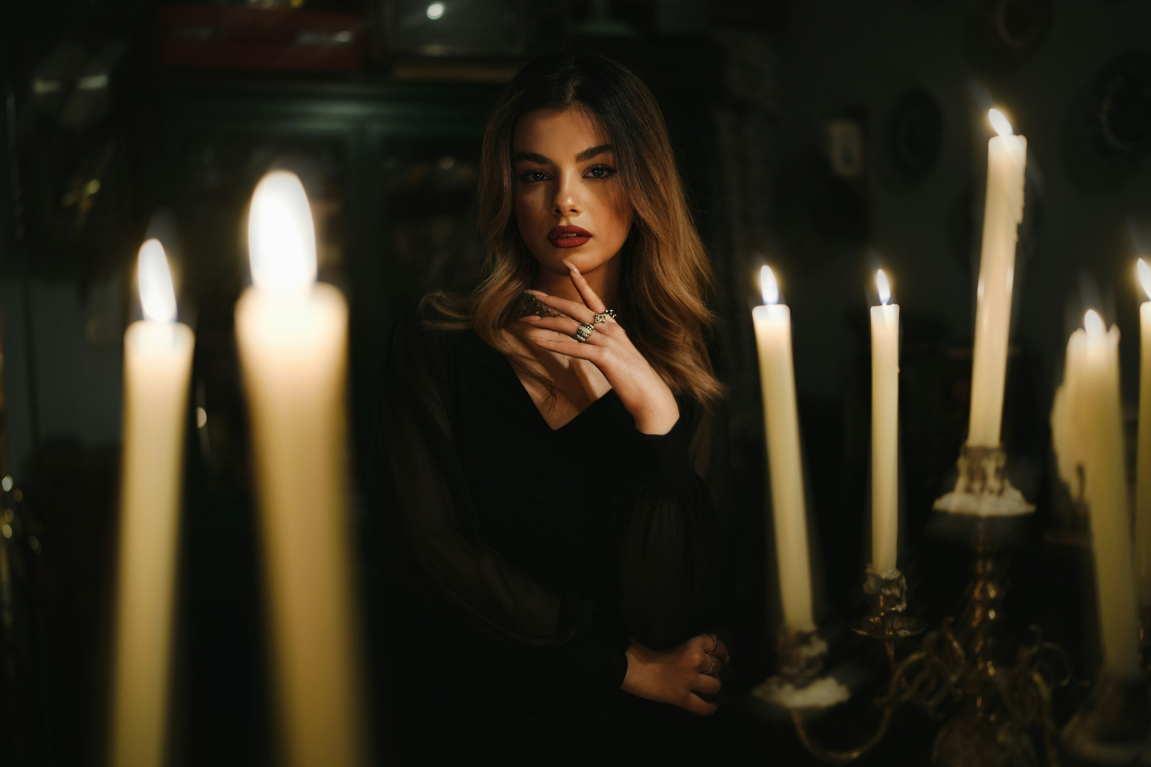 Una donna in abito nero circondata da candele accese in una stanza buia