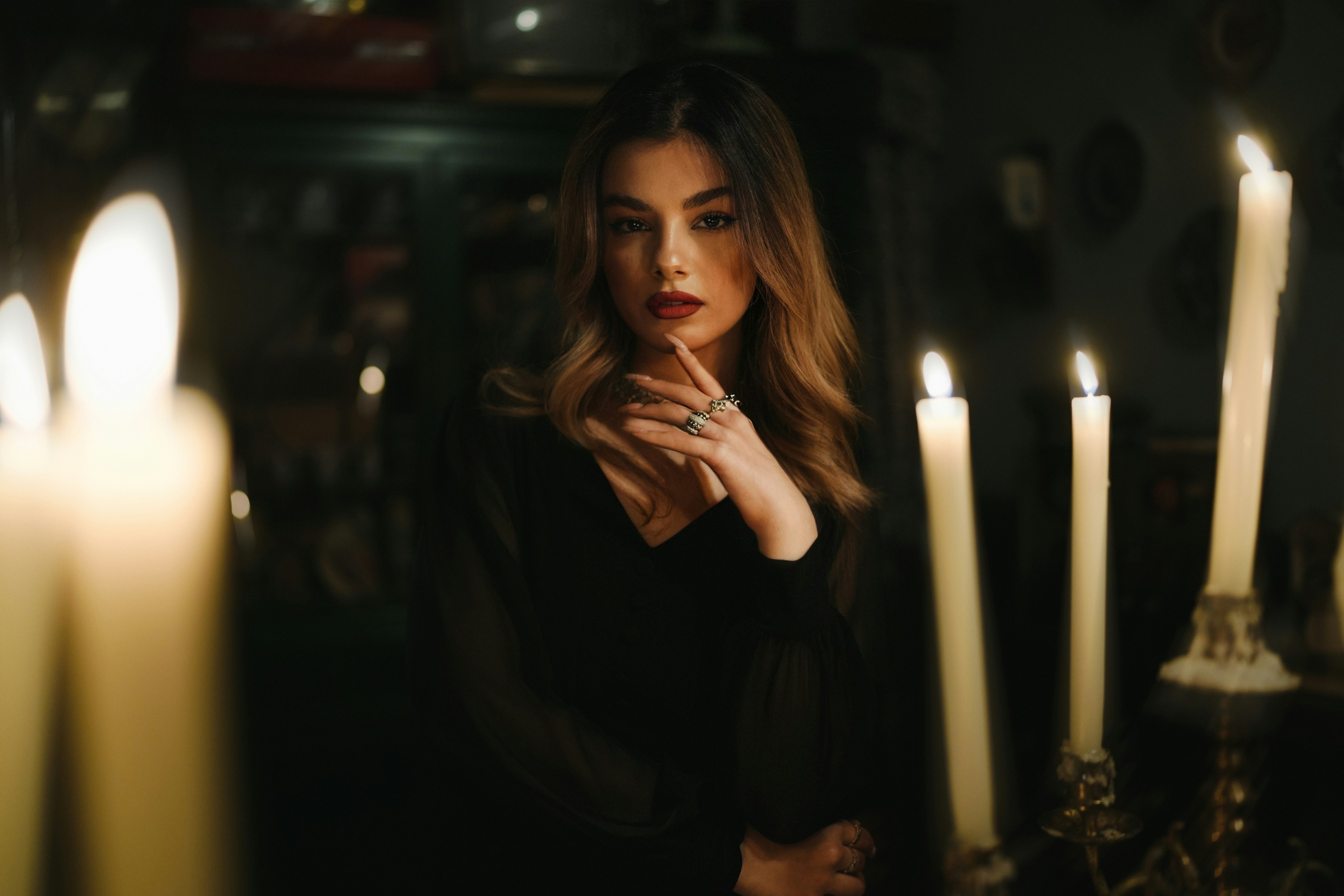 Una donna in un abito nero con anelli, illuminata da candele accese