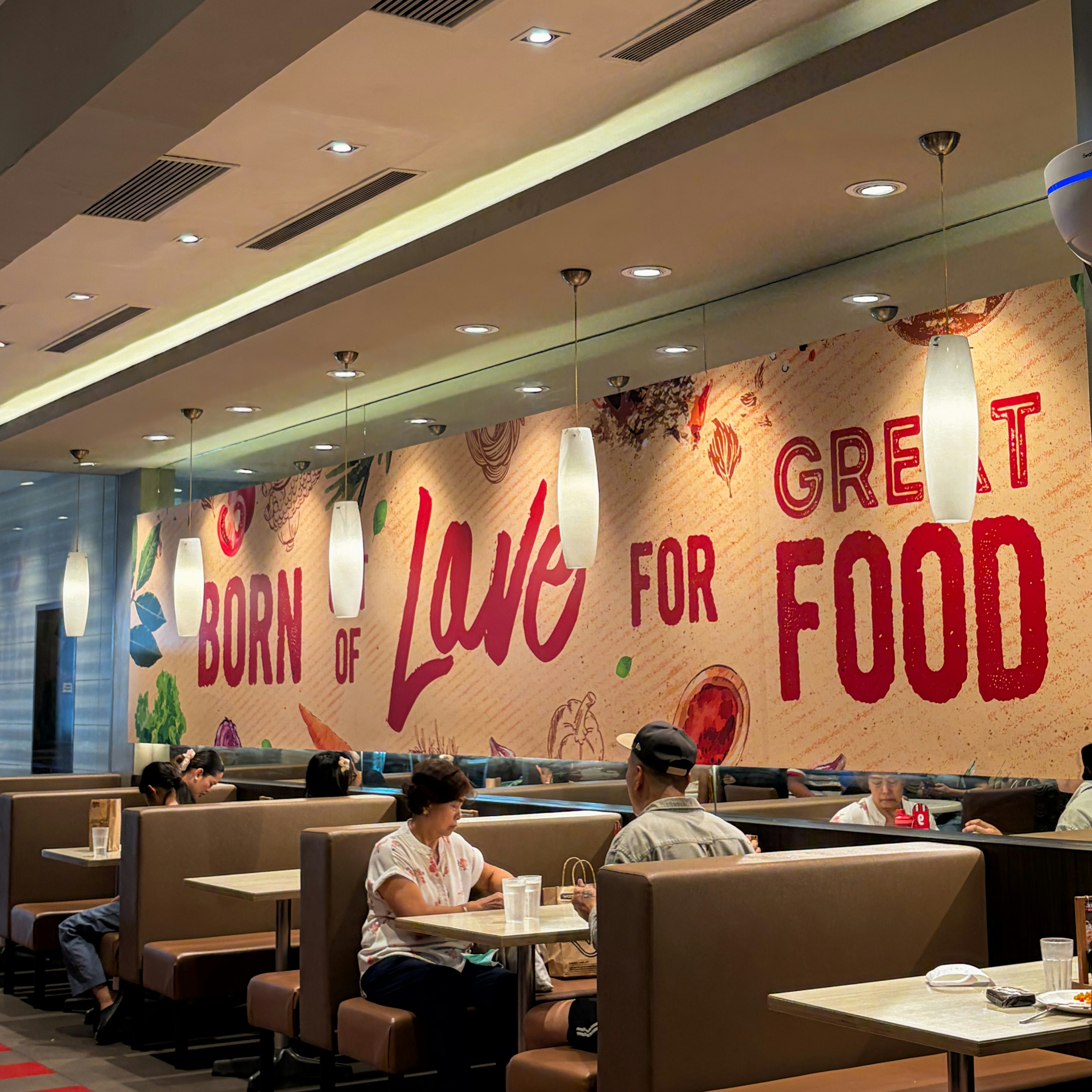 People dining in booths beneath a wall mural reading Born of Love for Food