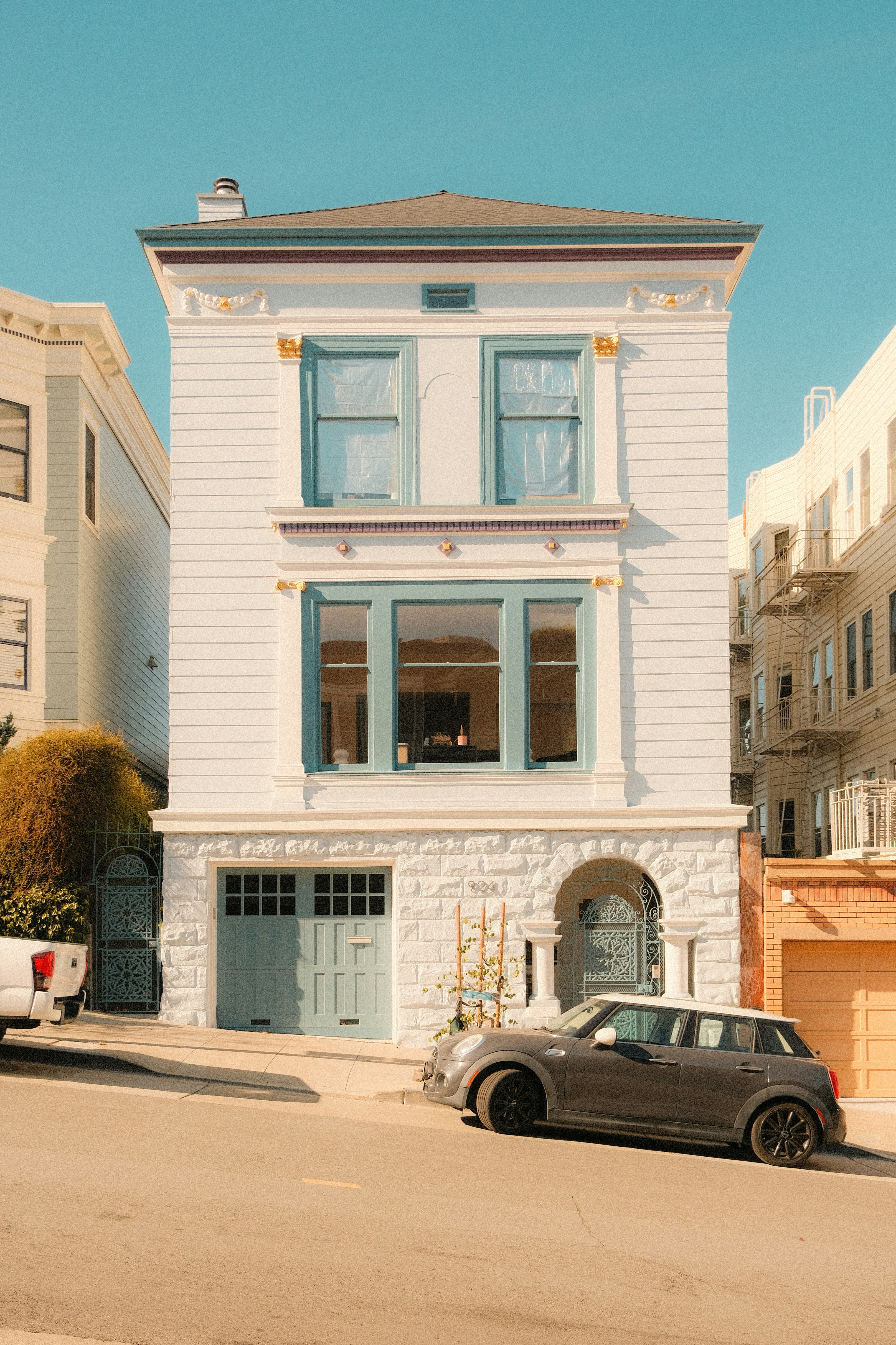 A white Victorian house with blue trim on a steep San Francisco street