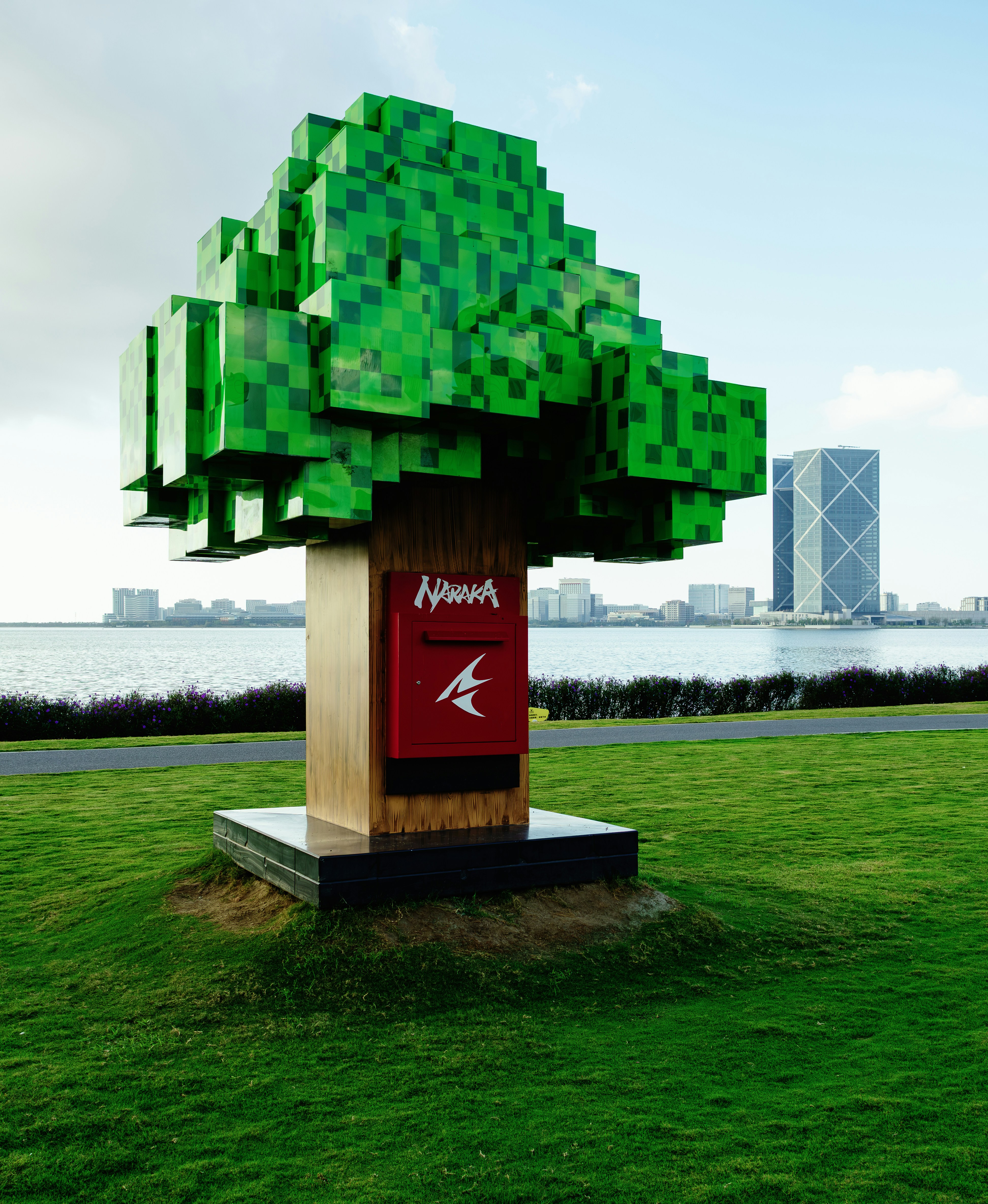 Una escultura de árbol verde pixelada con un buzón rojo en el césped de un parque