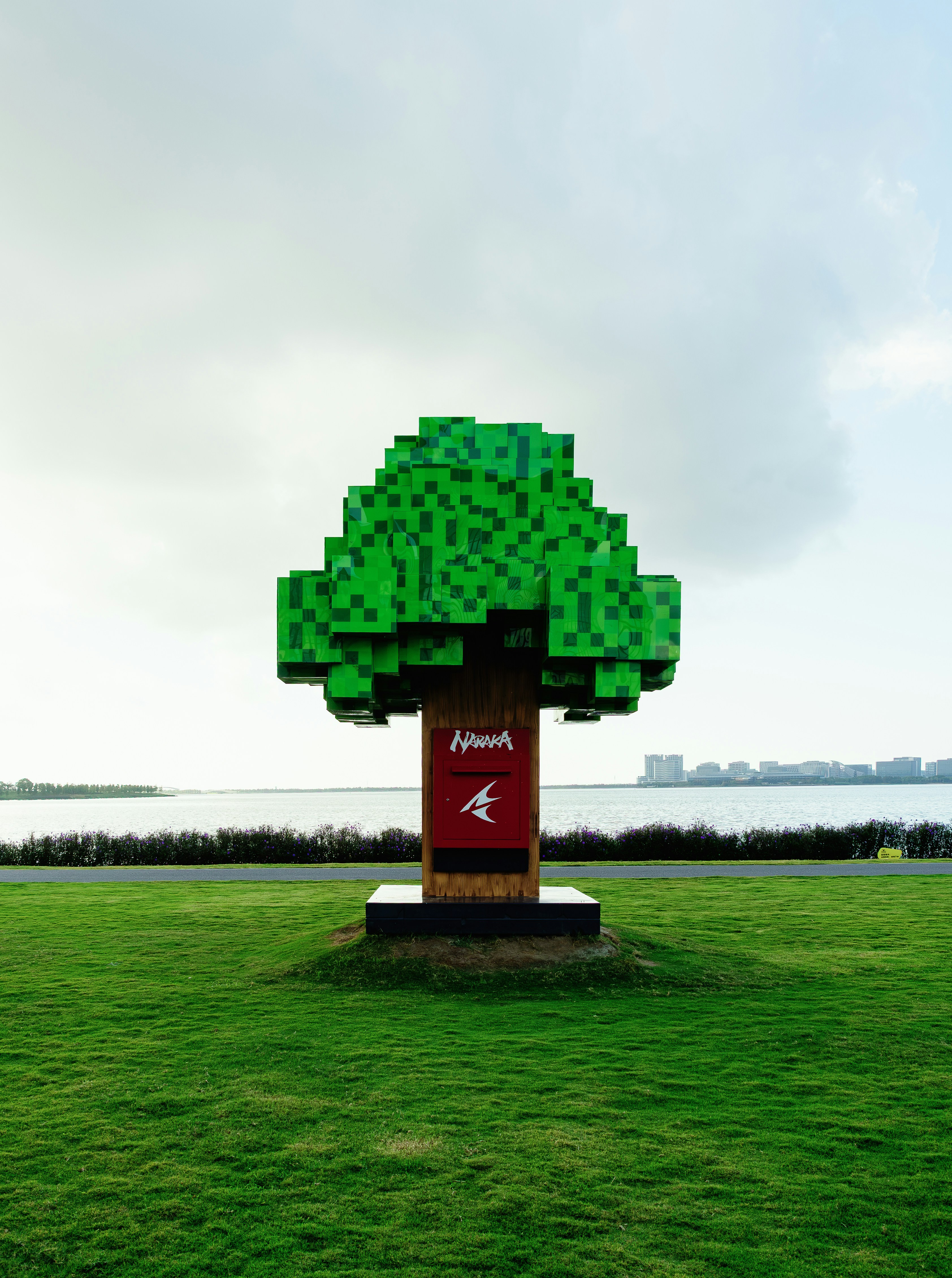 Una escultura de árbol verde pixelada con un tronco de buzón rojo sobre un césped cubierto de césped
