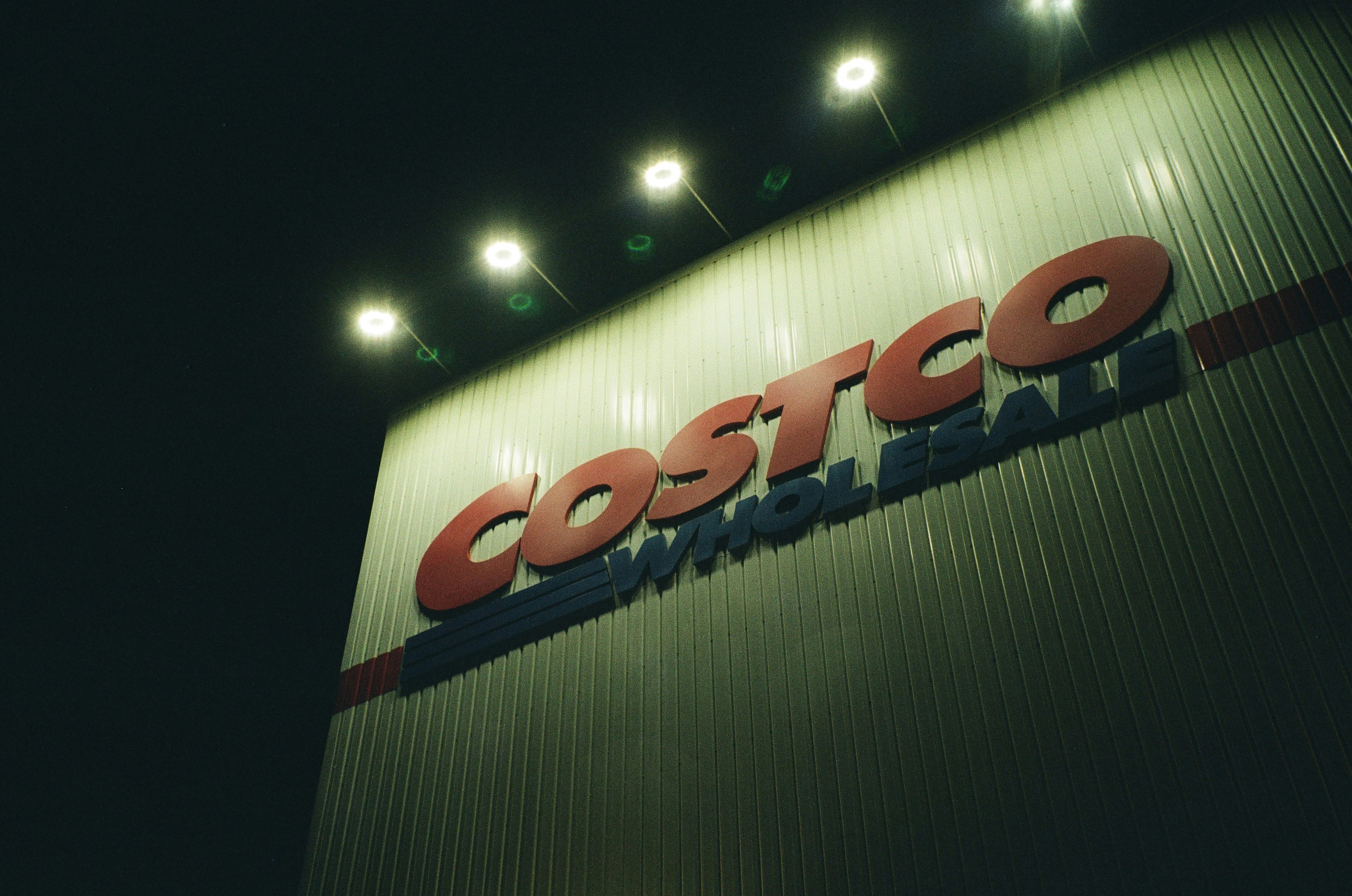 Why Investors Are Reading Between the Lines — The Costco Wholesale sign on a corrugated metal wall at night under bright lights