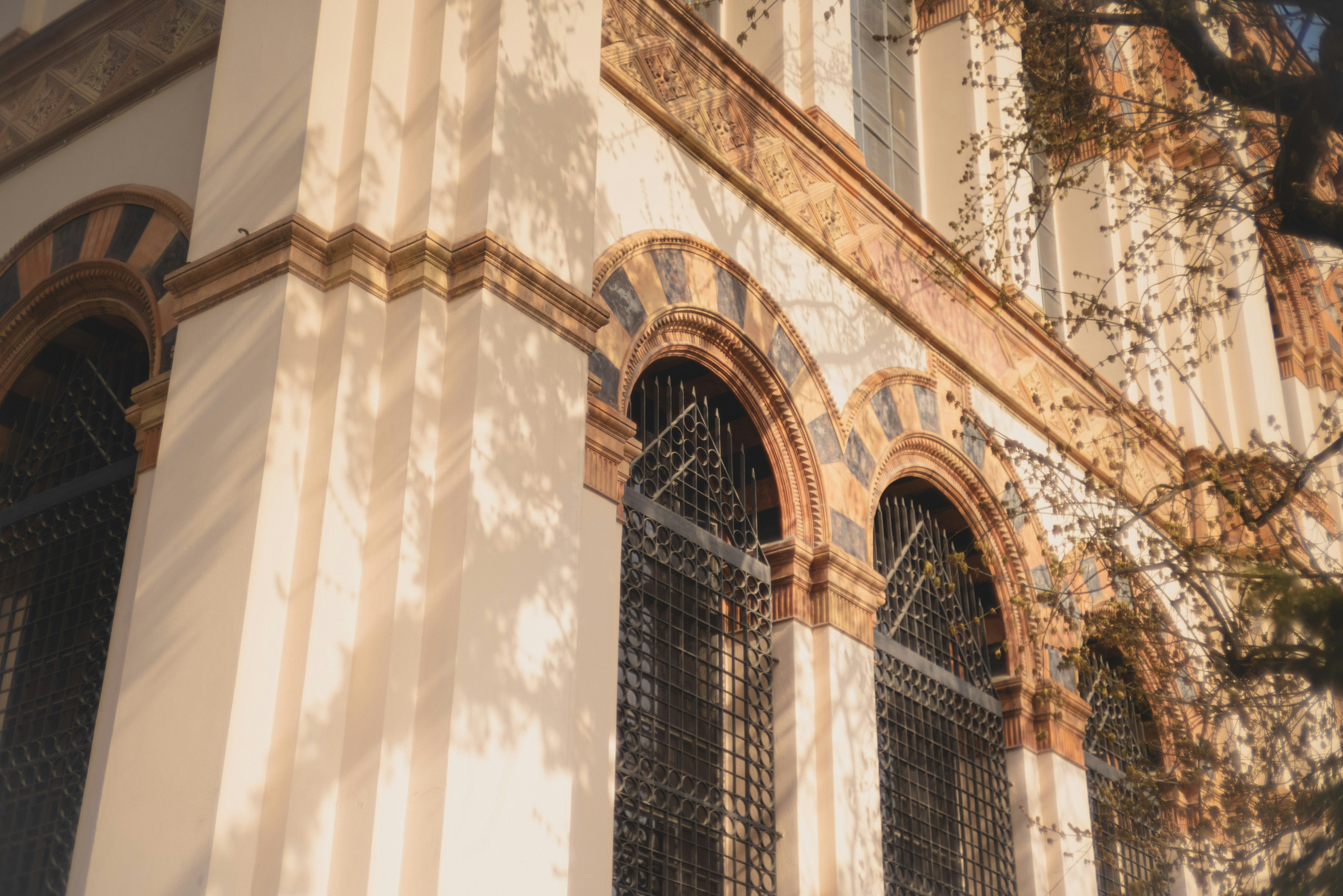 Arched windows with metal grilles on a light-colored building facade in warm light