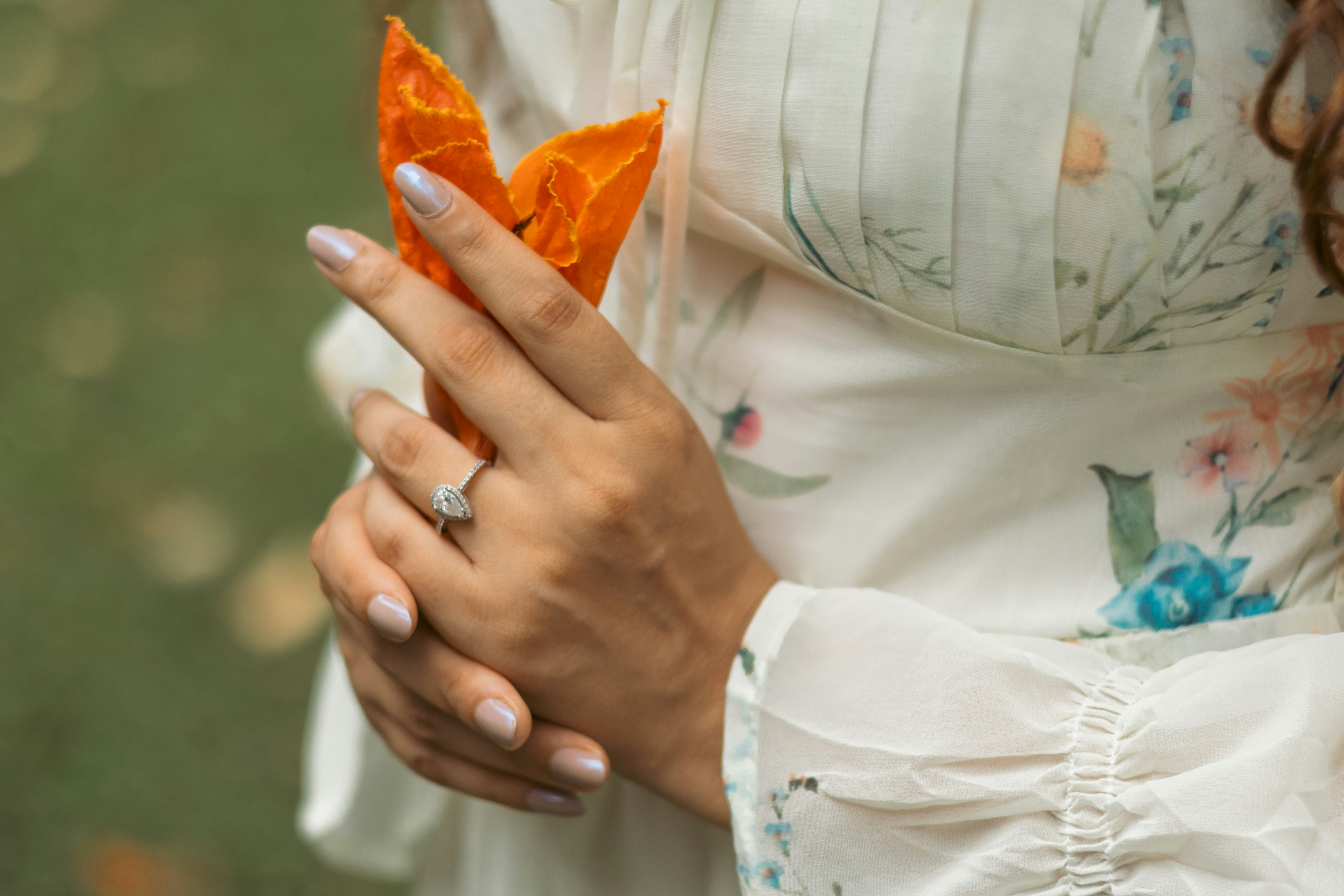 A person wearing a floral dress holding an orange flower with a diamond ring