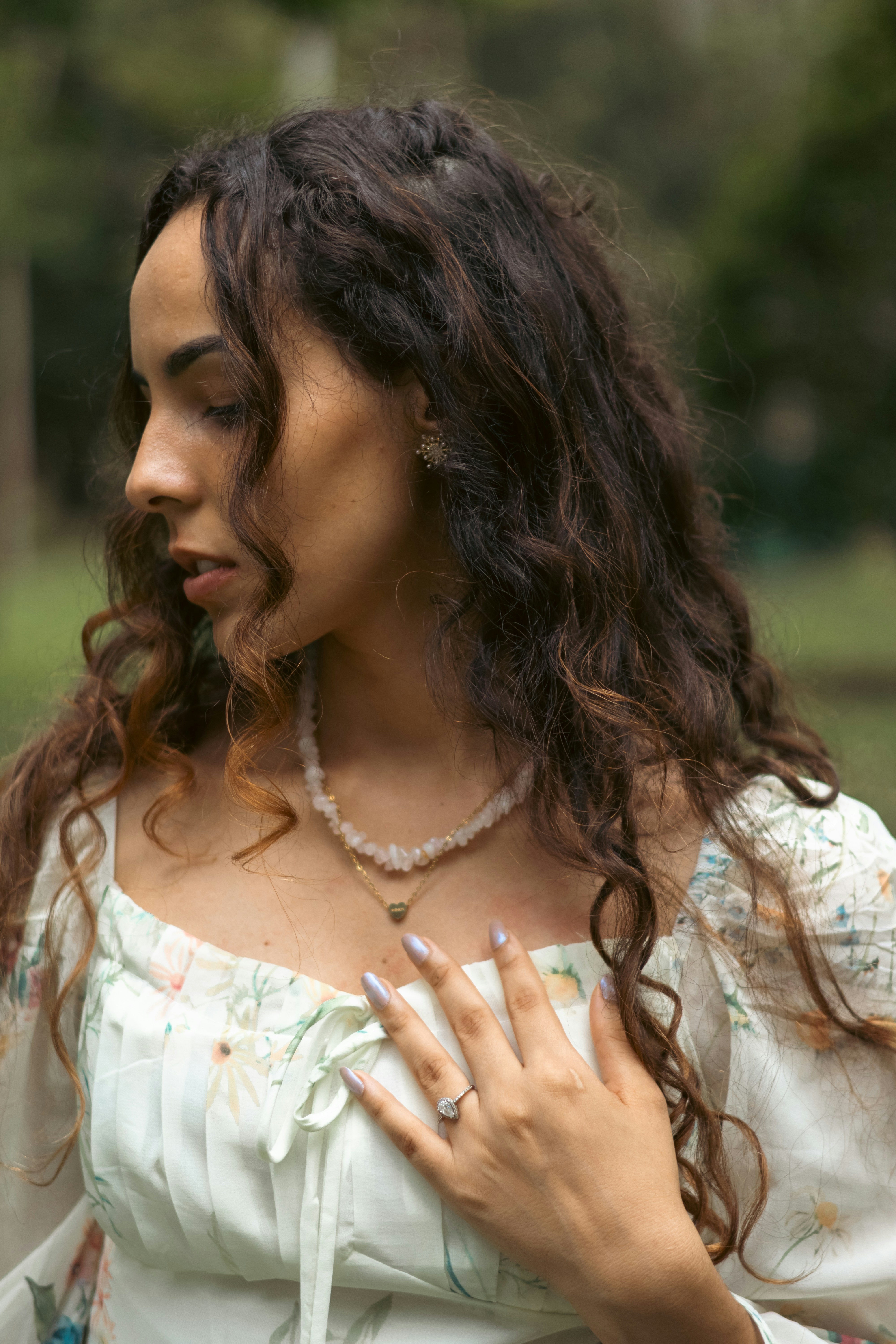 A woman with long curly hair wearing a floral dress and layered necklaces