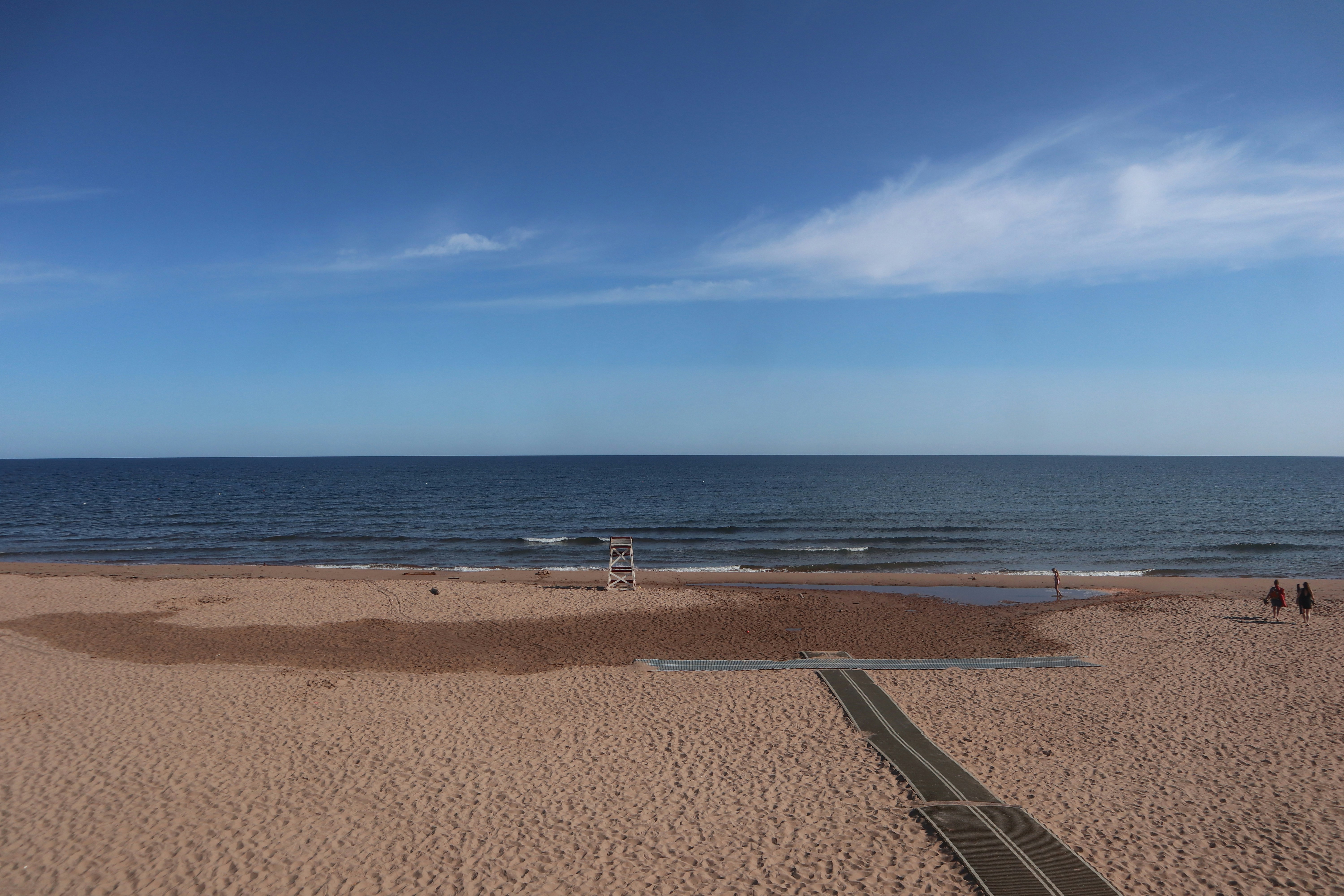 A sandy beach with a lifeguard chair and a walkway leading to the ocean