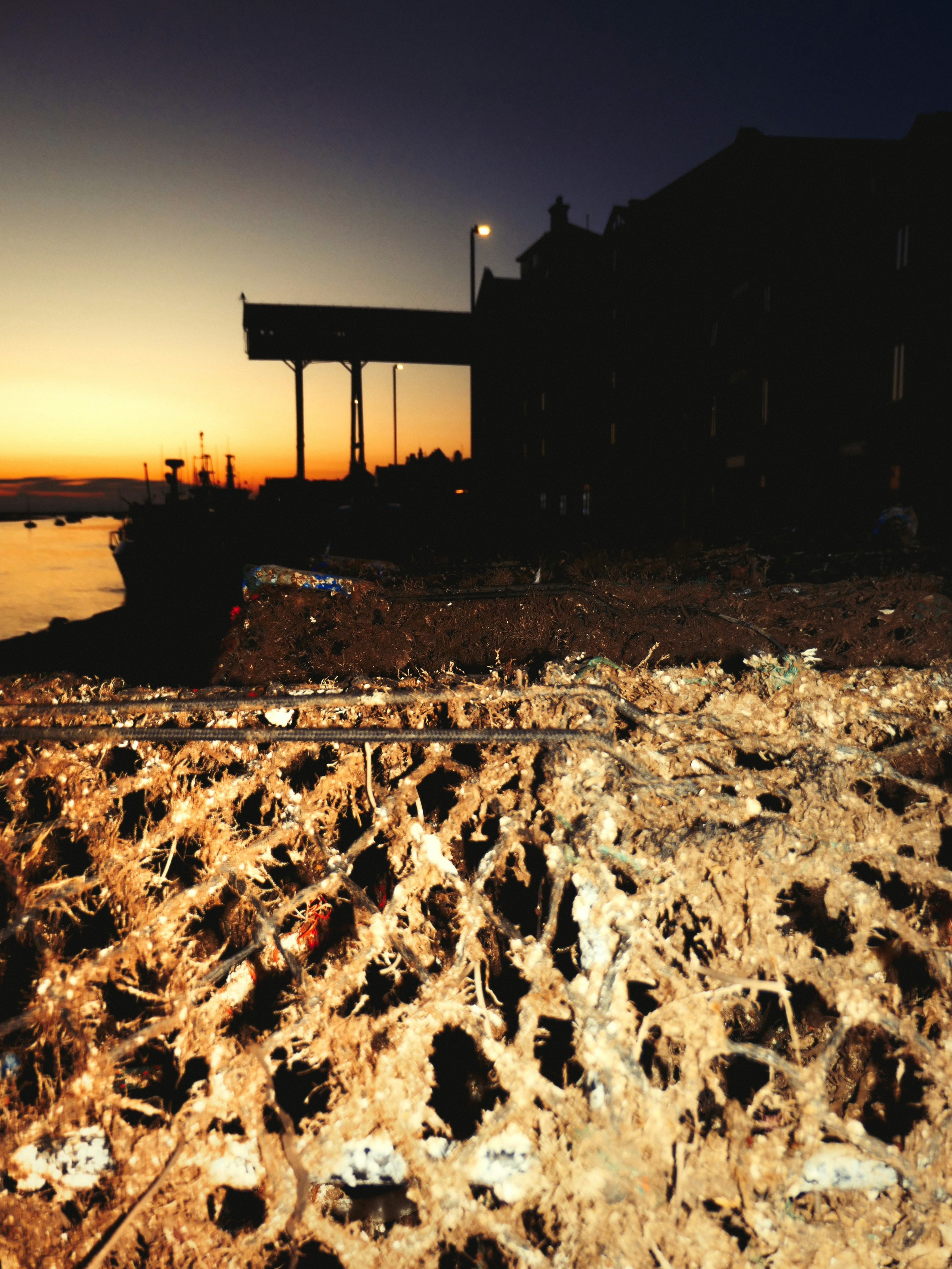 A weathered fishing net in the foreground against a dark harbor at golden hour
