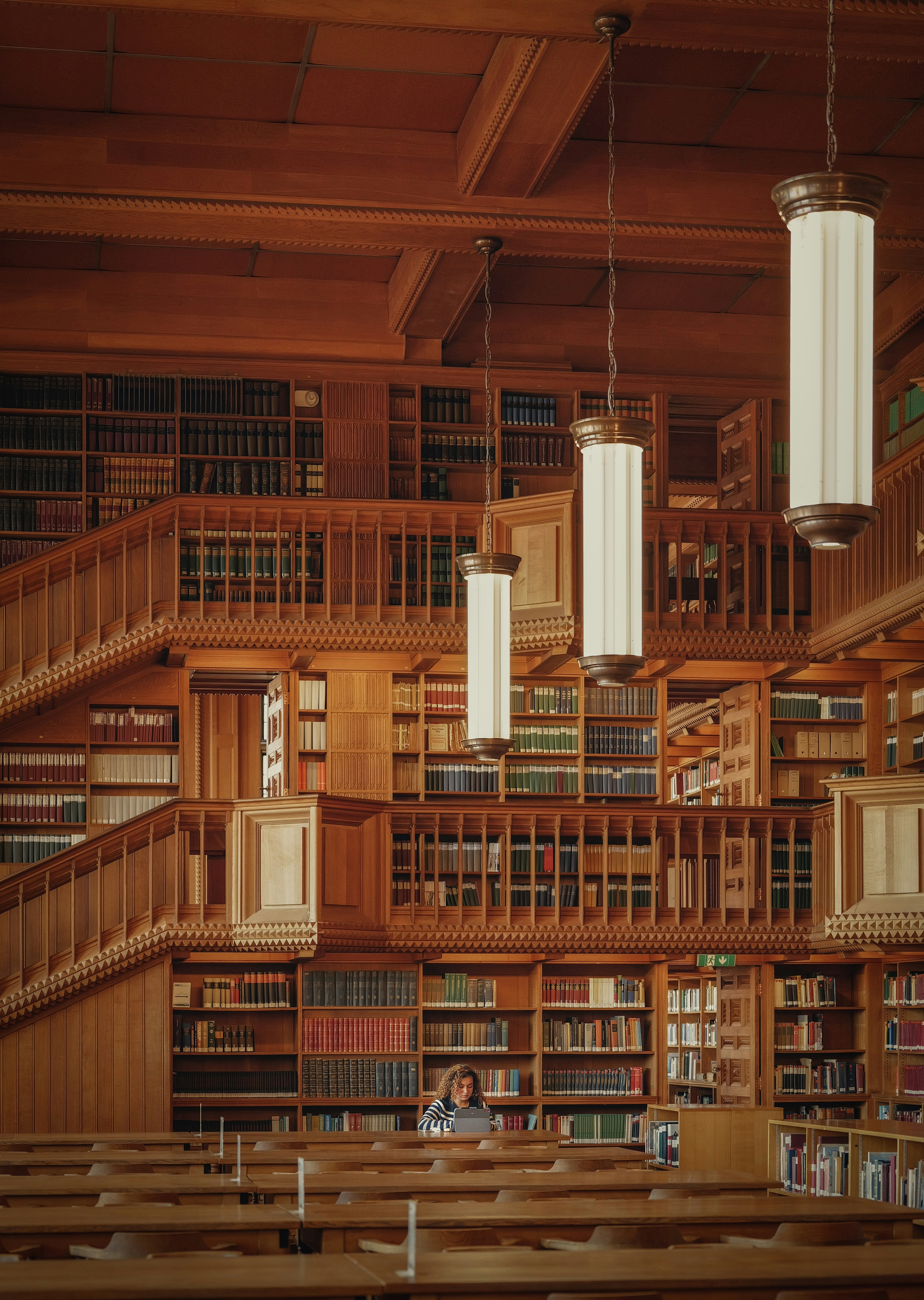 A person working on a laptop in a large wooden library with tiered bookshelves