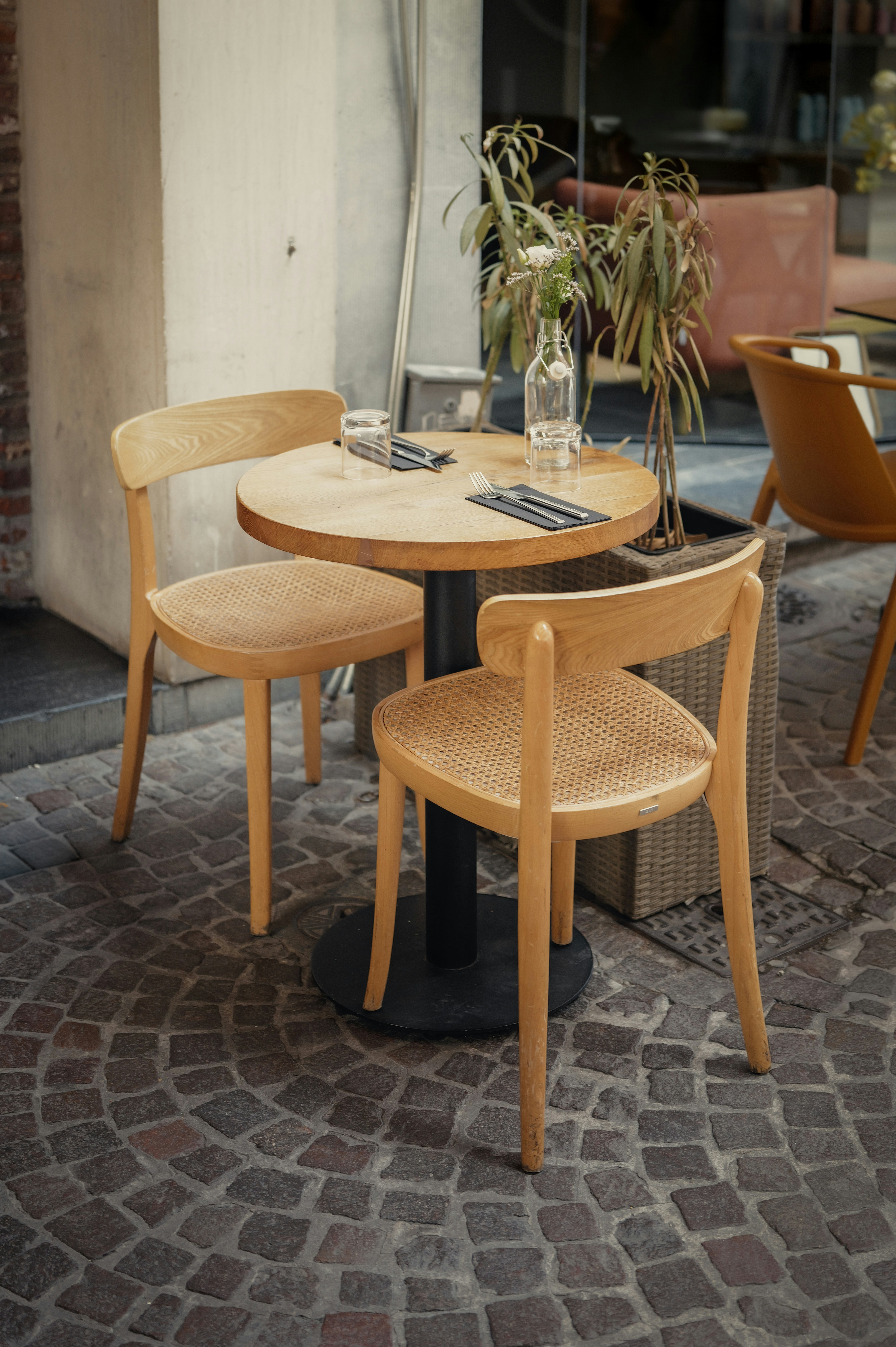 A round wooden table with two chairs on a cobblestone patio