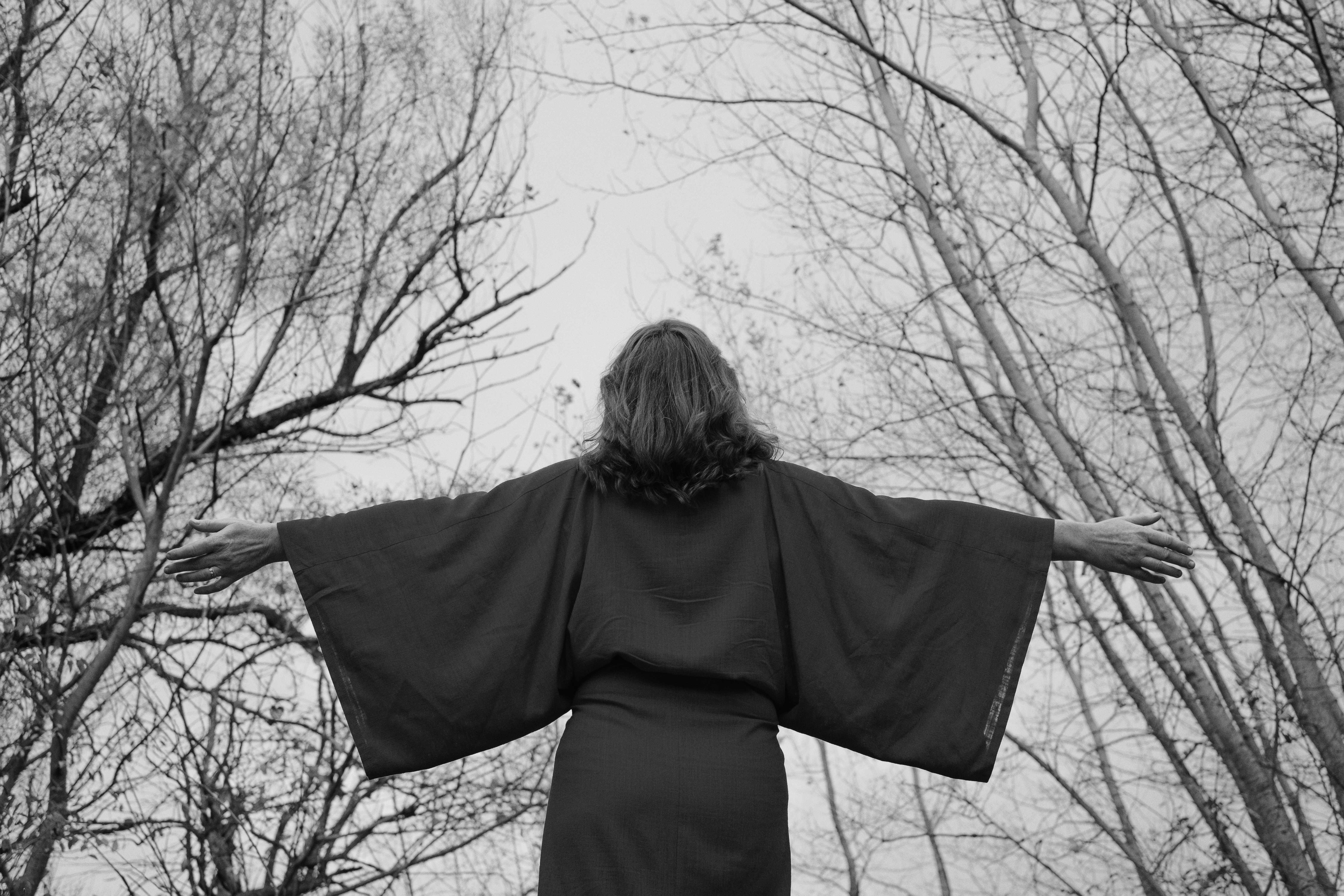 A person in a kimono with arms outstretched among bare winter trees