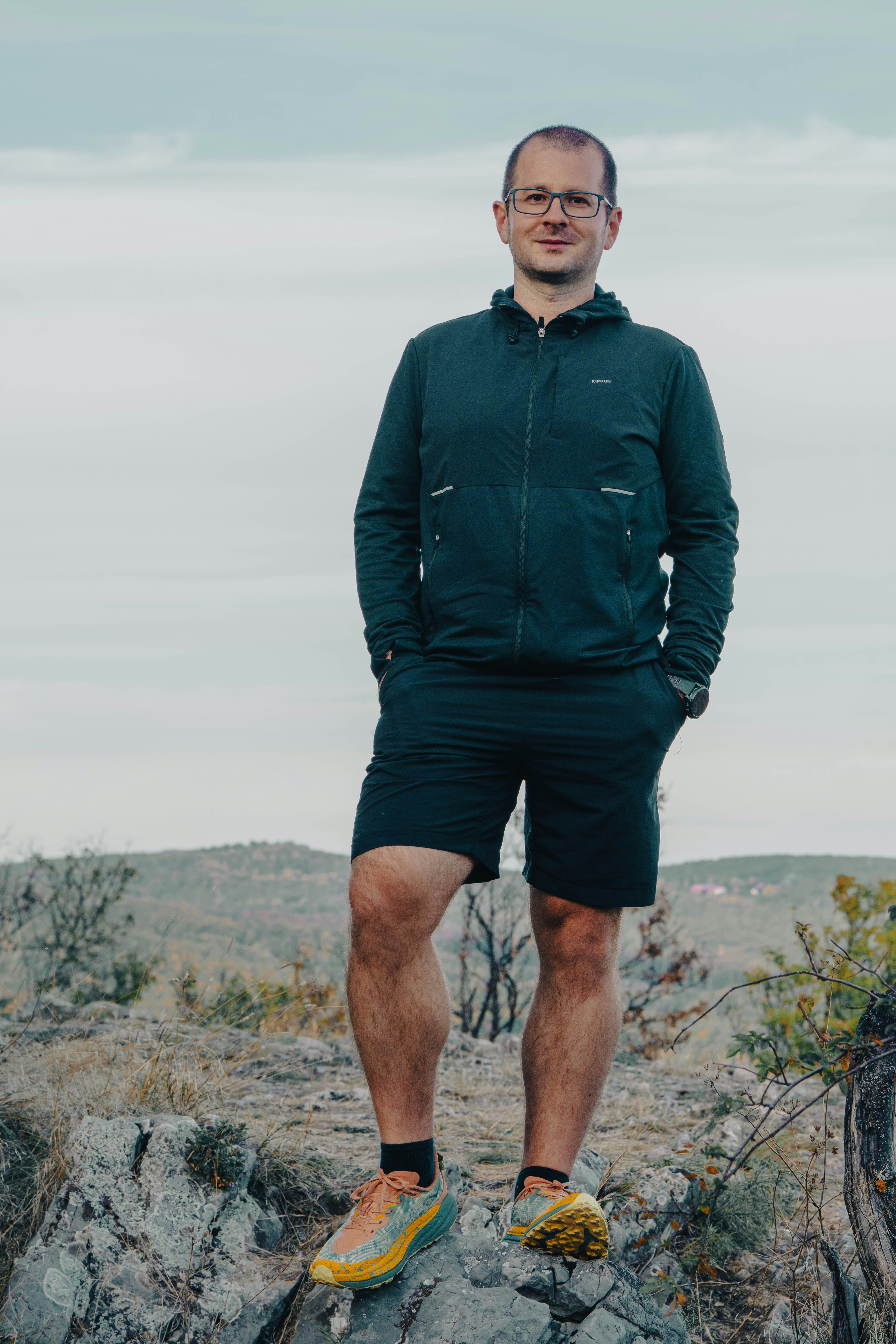A man in a dark jacket and shorts on a rocky hillside