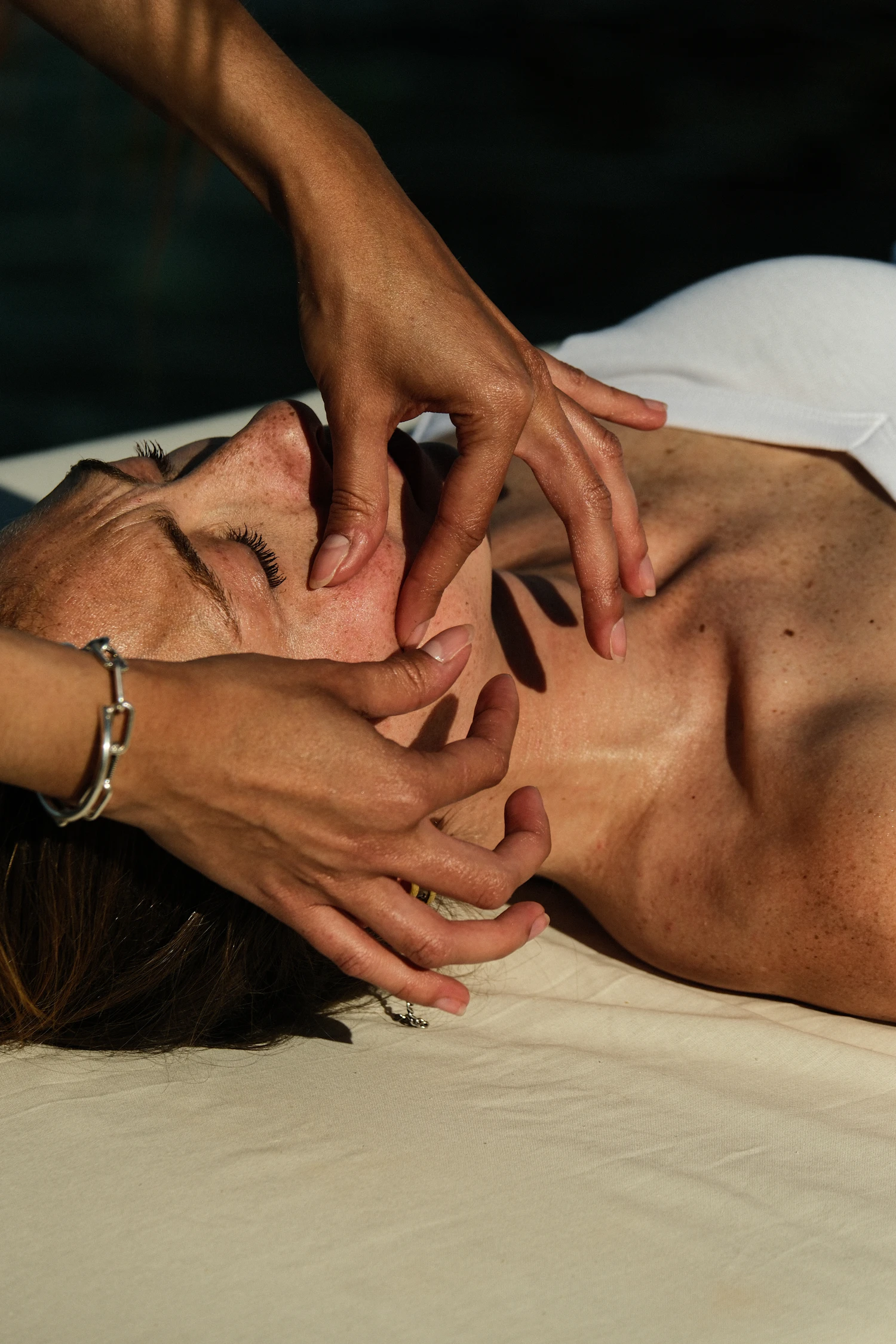 Hands working along a jawline in deep green shadow