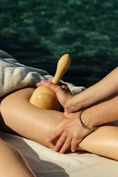 A person using a wooden massage tool on a leg near water