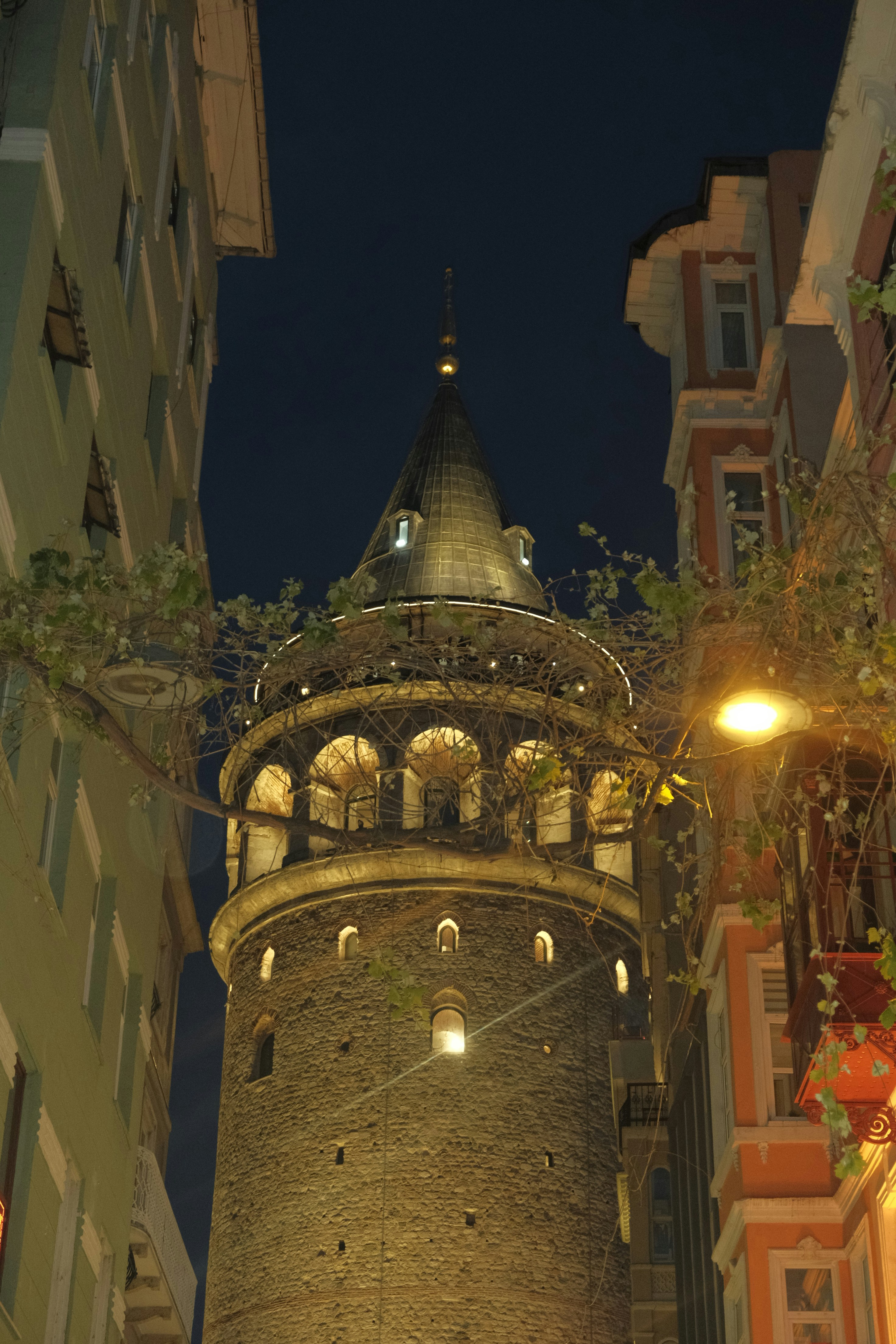 The Galata Tower illuminated at night between narrow buildings in Istanbul