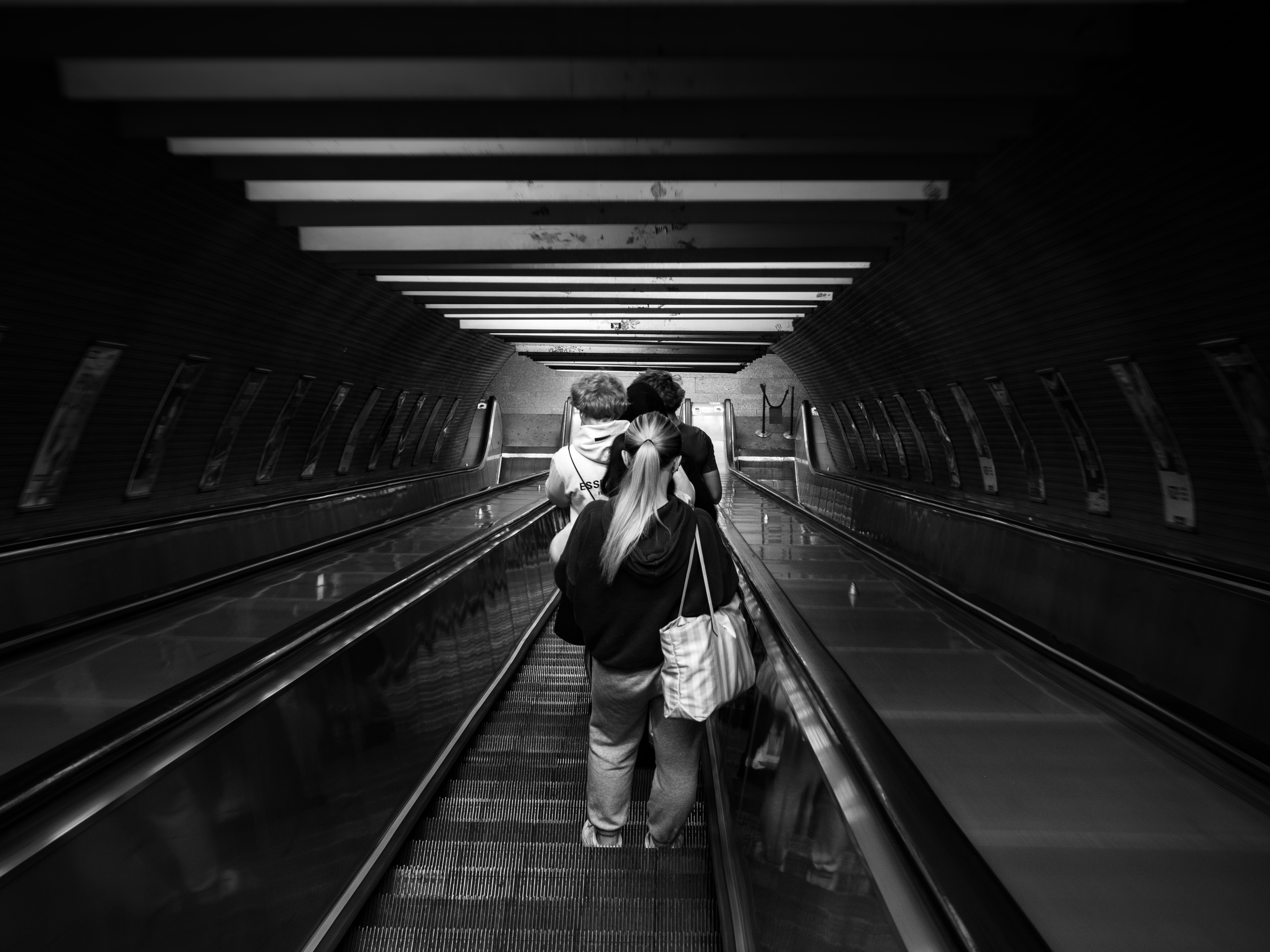 Black and white photo of people riding an escalator in a station tunnel