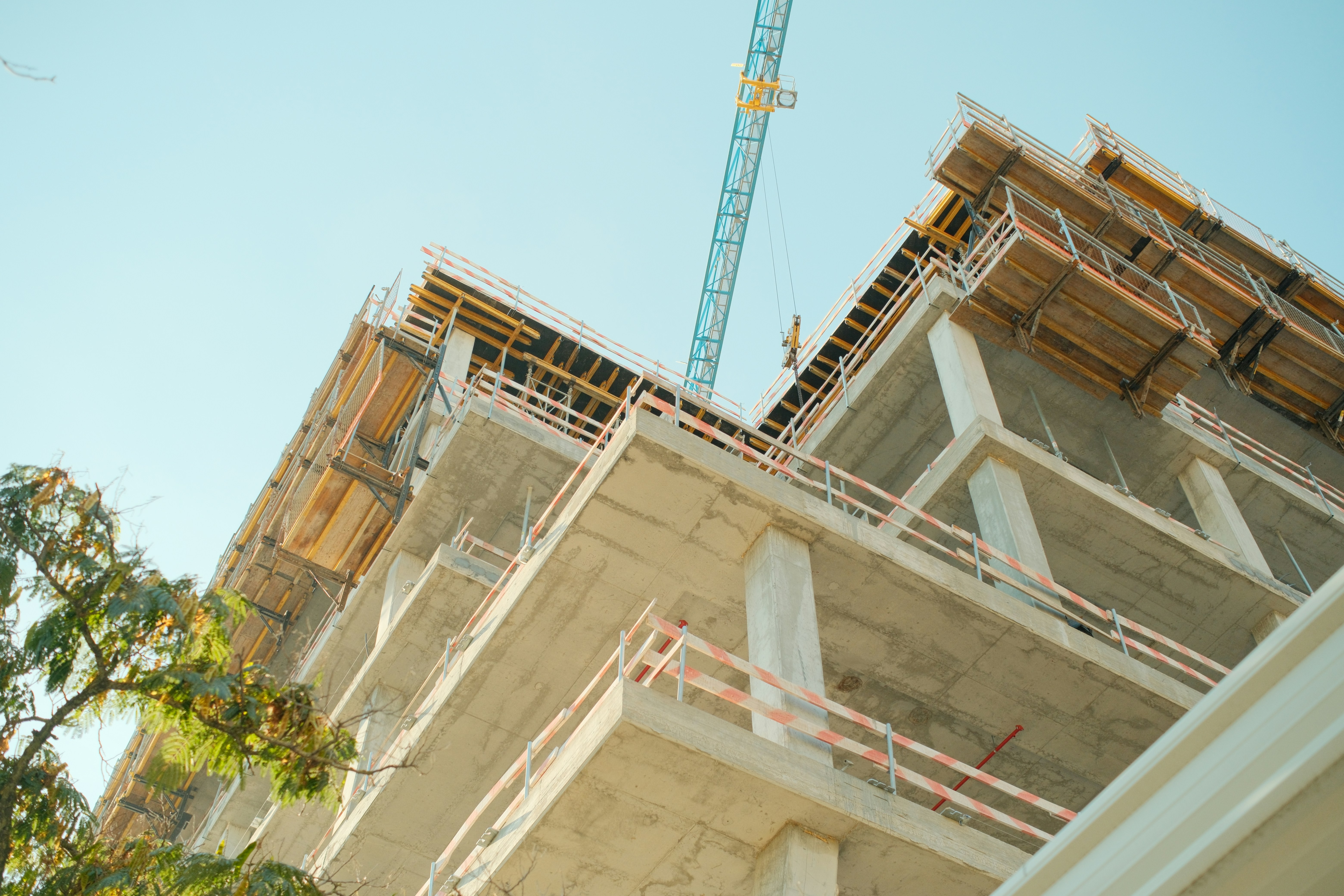 A concrete building under construction with a blue crane against a clear sky