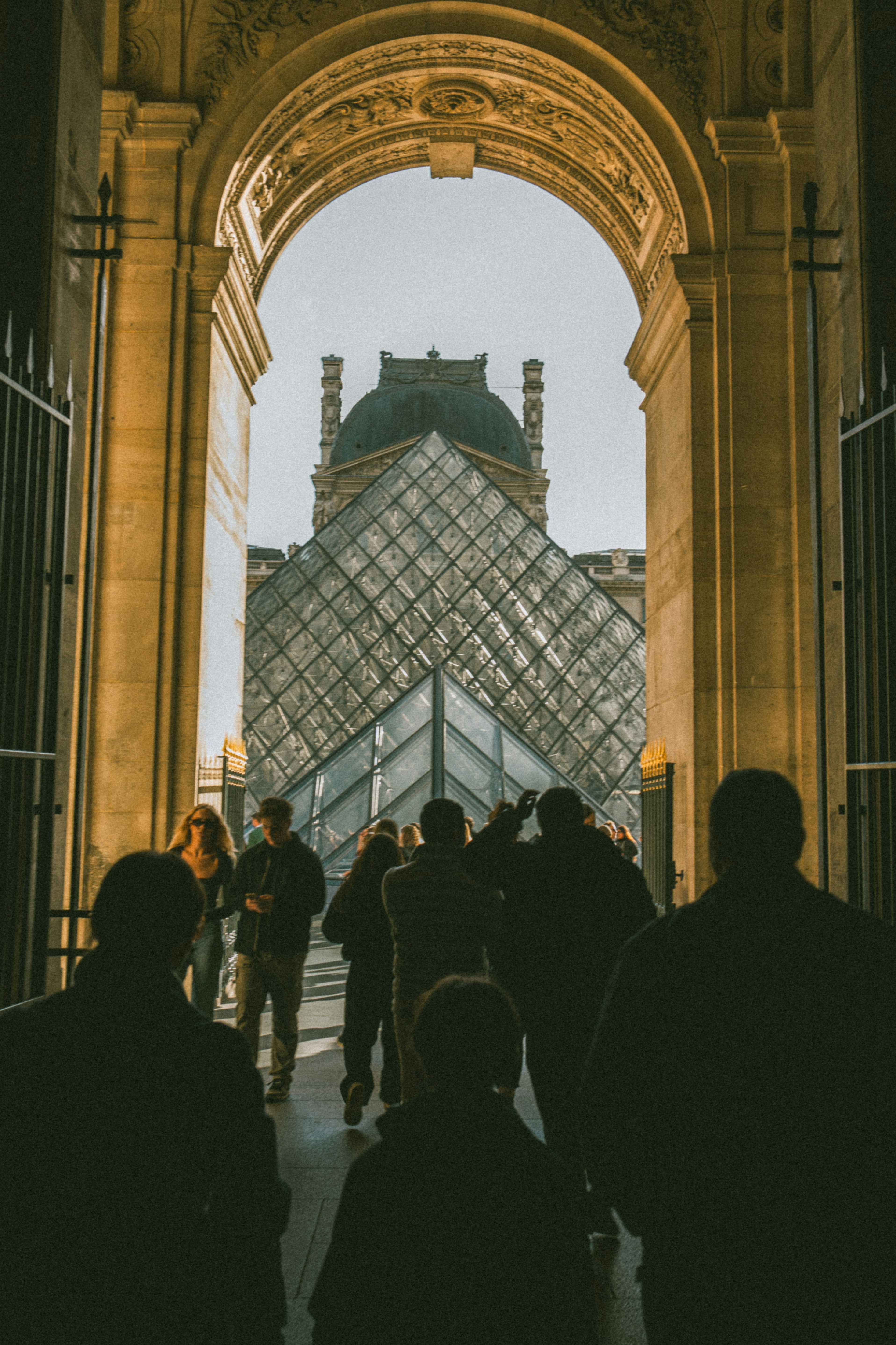 People walking through a stone archway toward the Louvre Pyramid in Paris