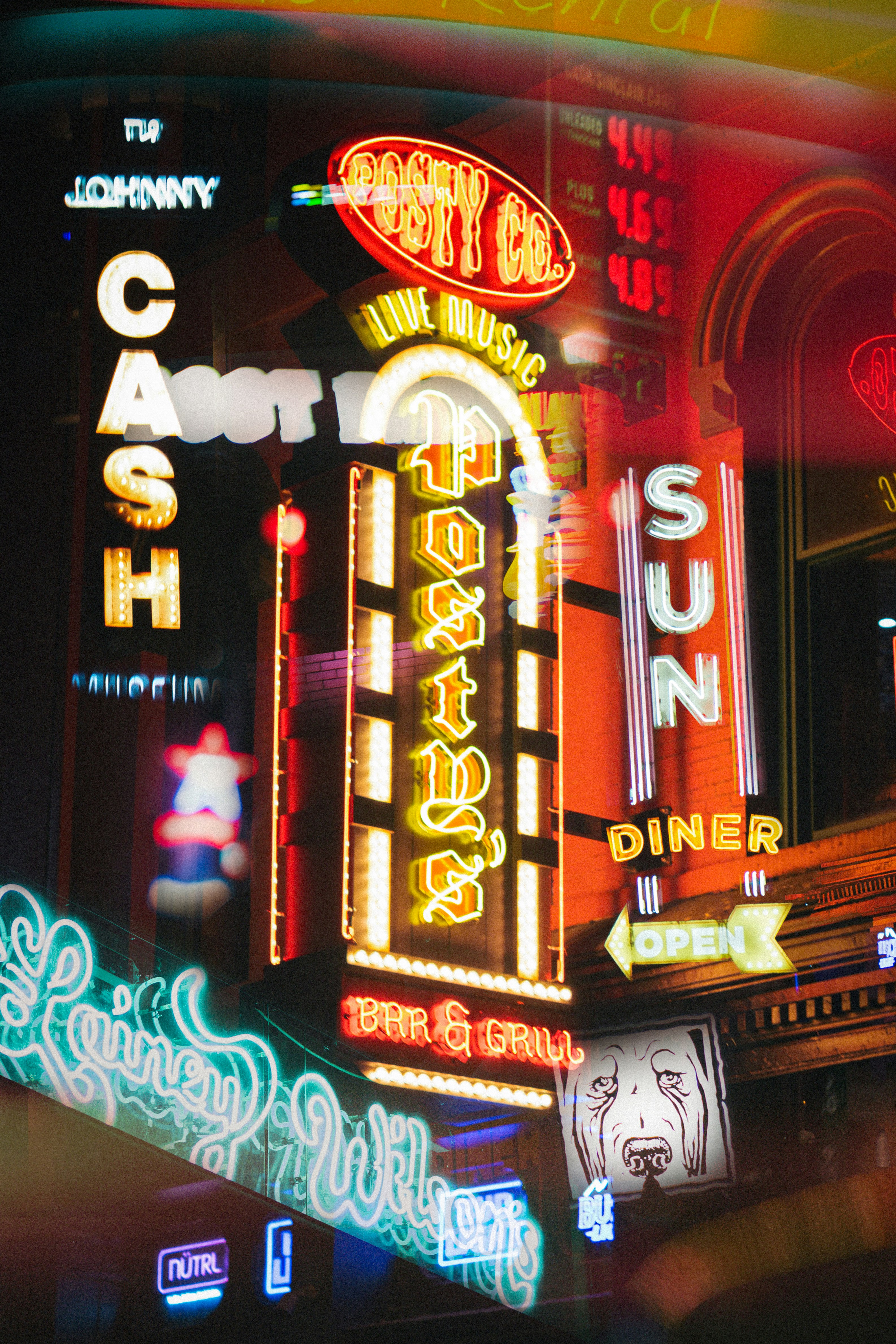 Bright neon signs for a bar and grill reflected in a dark window