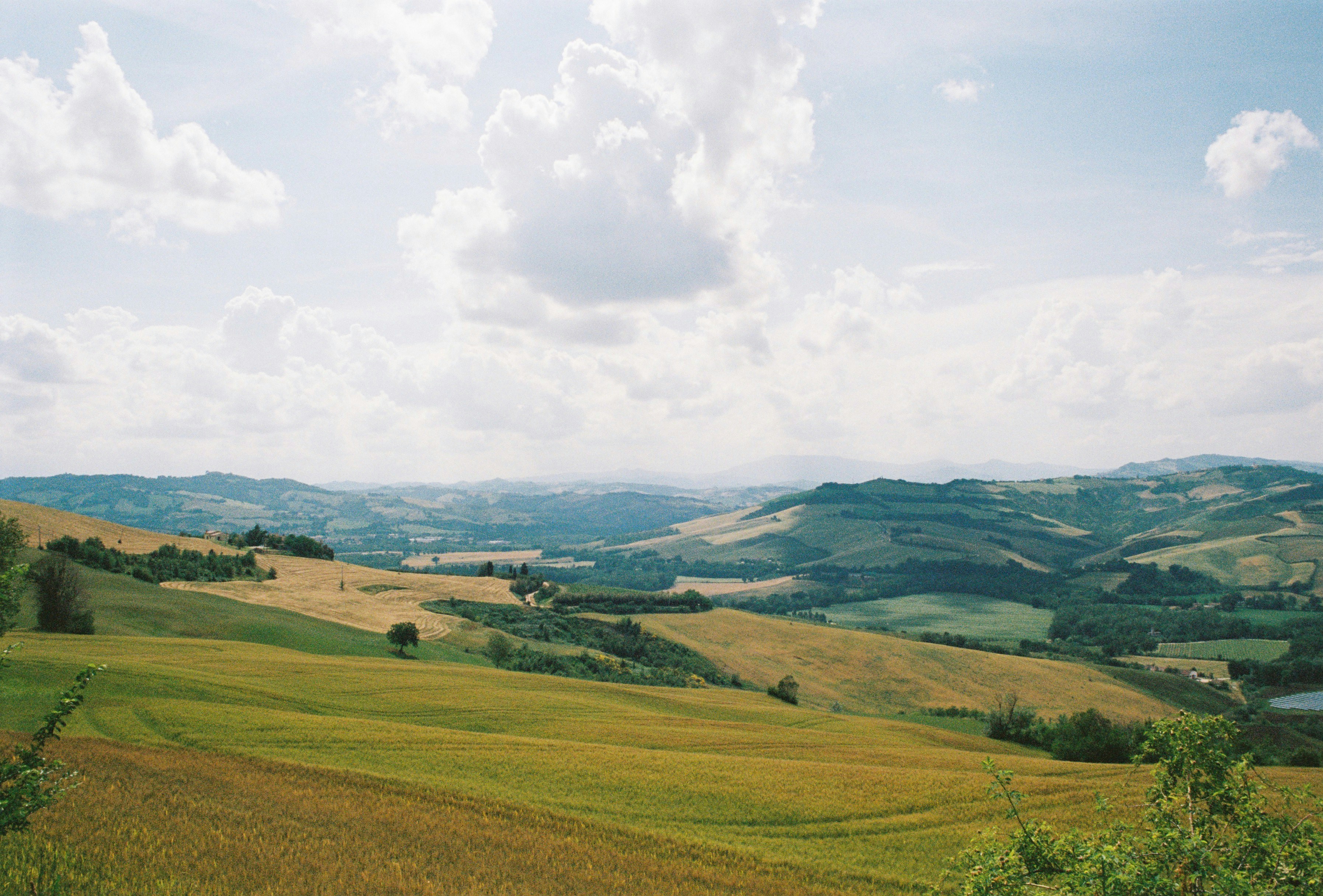 Rolling green and golden hills under a bright sky with scattered white clouds
