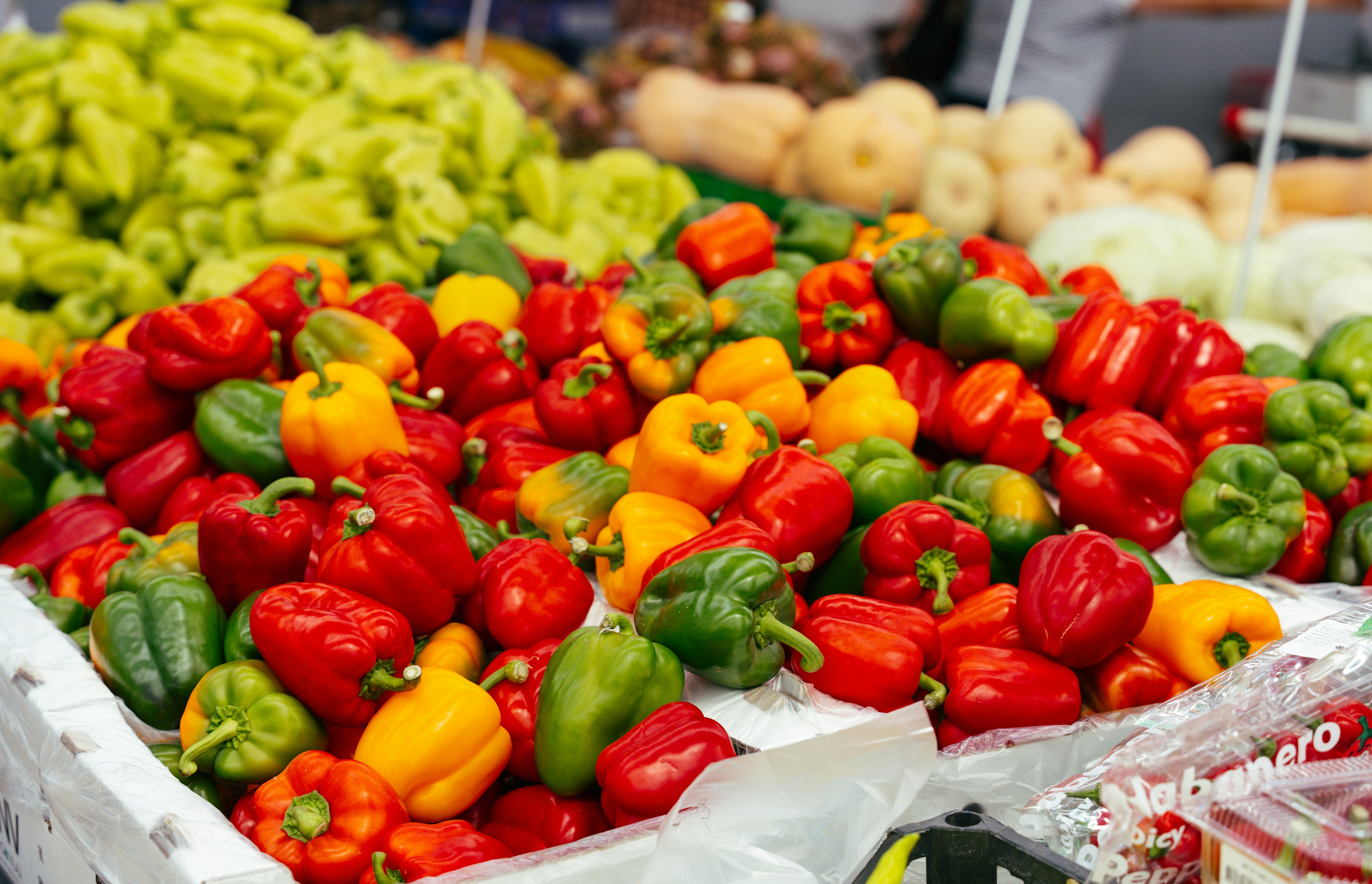 A large pile of fresh red, yellow, and green bell peppers at a market