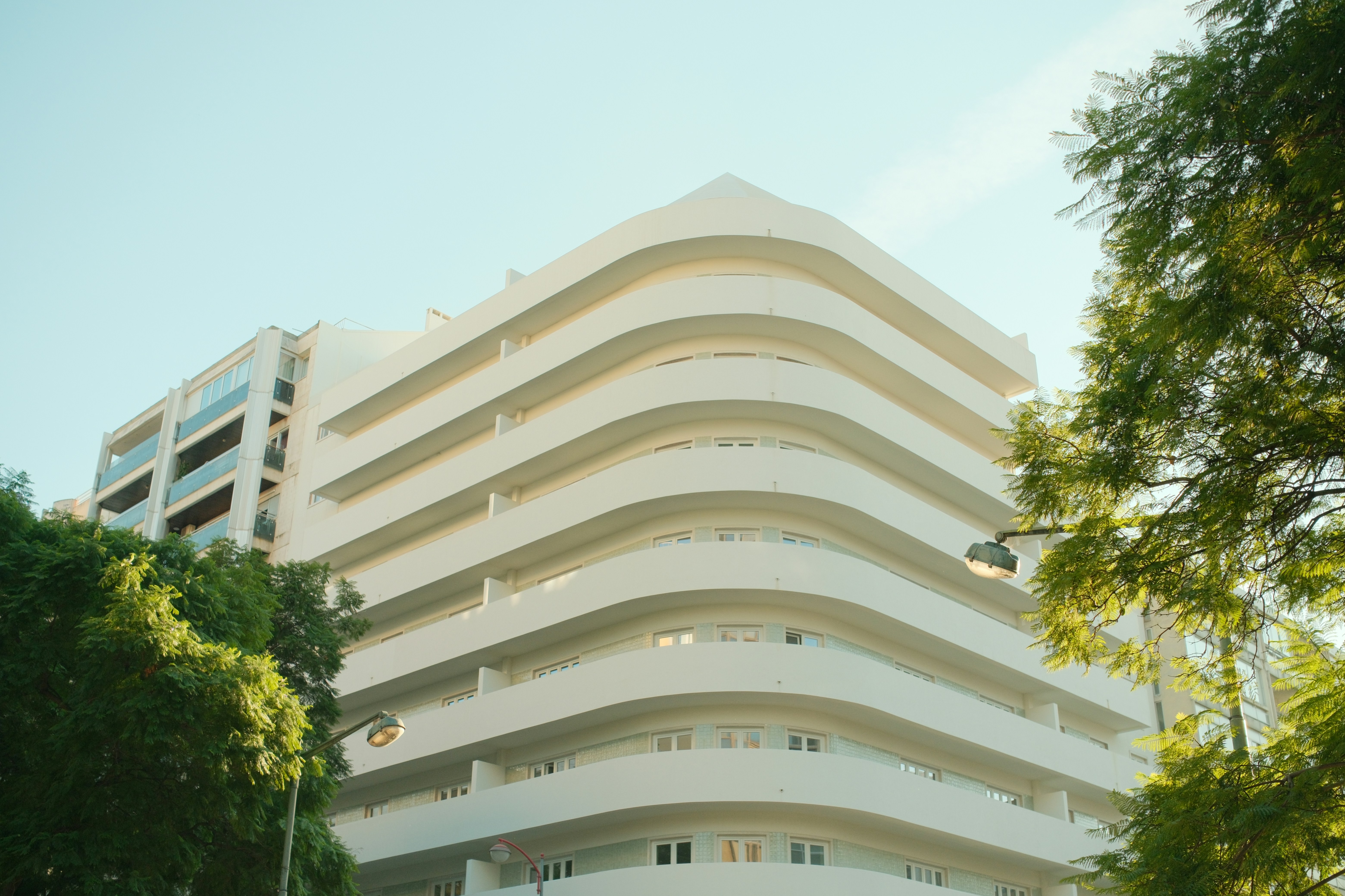 A white apartment building with curved balconies framed by green trees