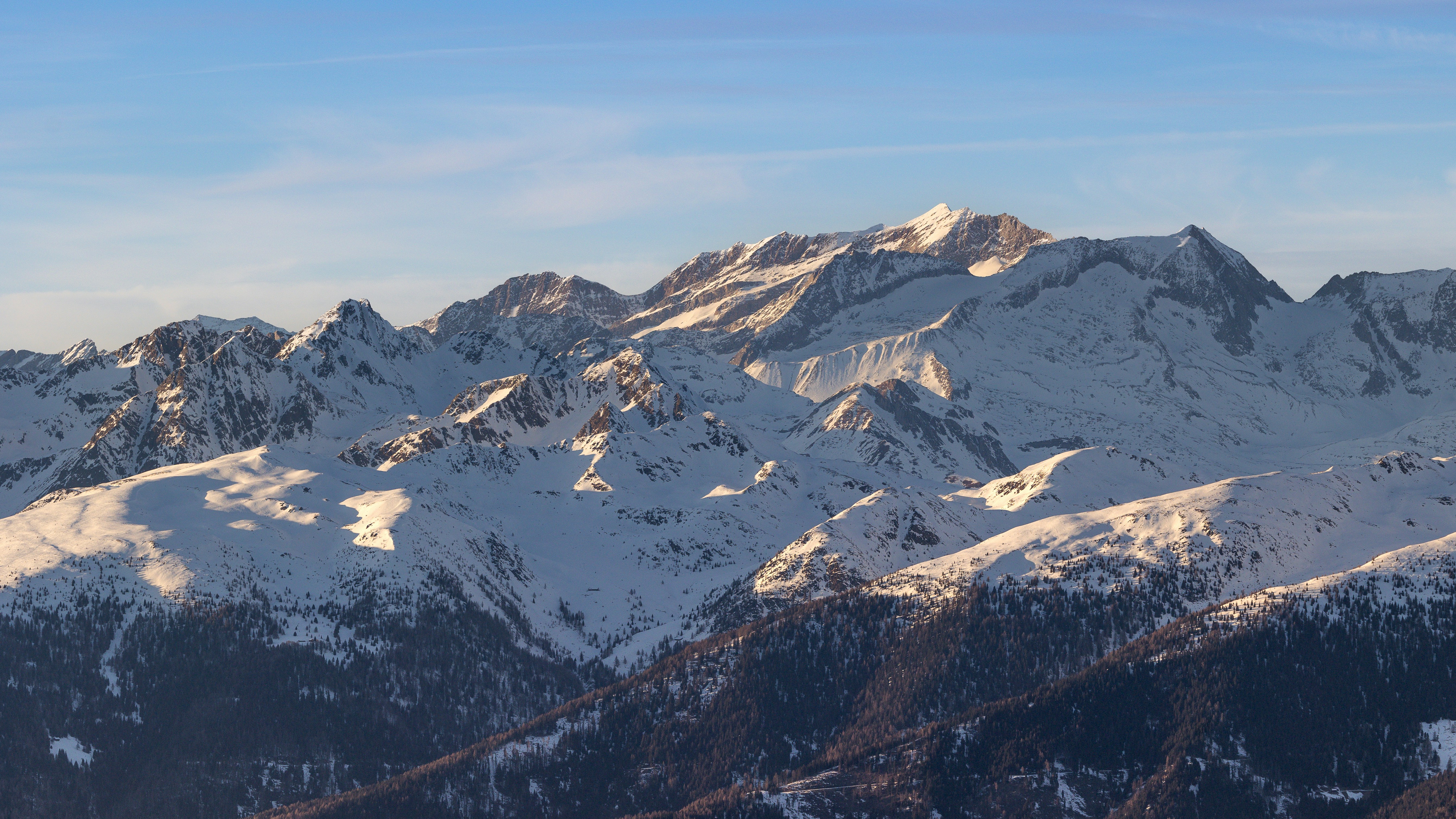 Snow-covered mountain peaks under a clear blue sky with golden hour light