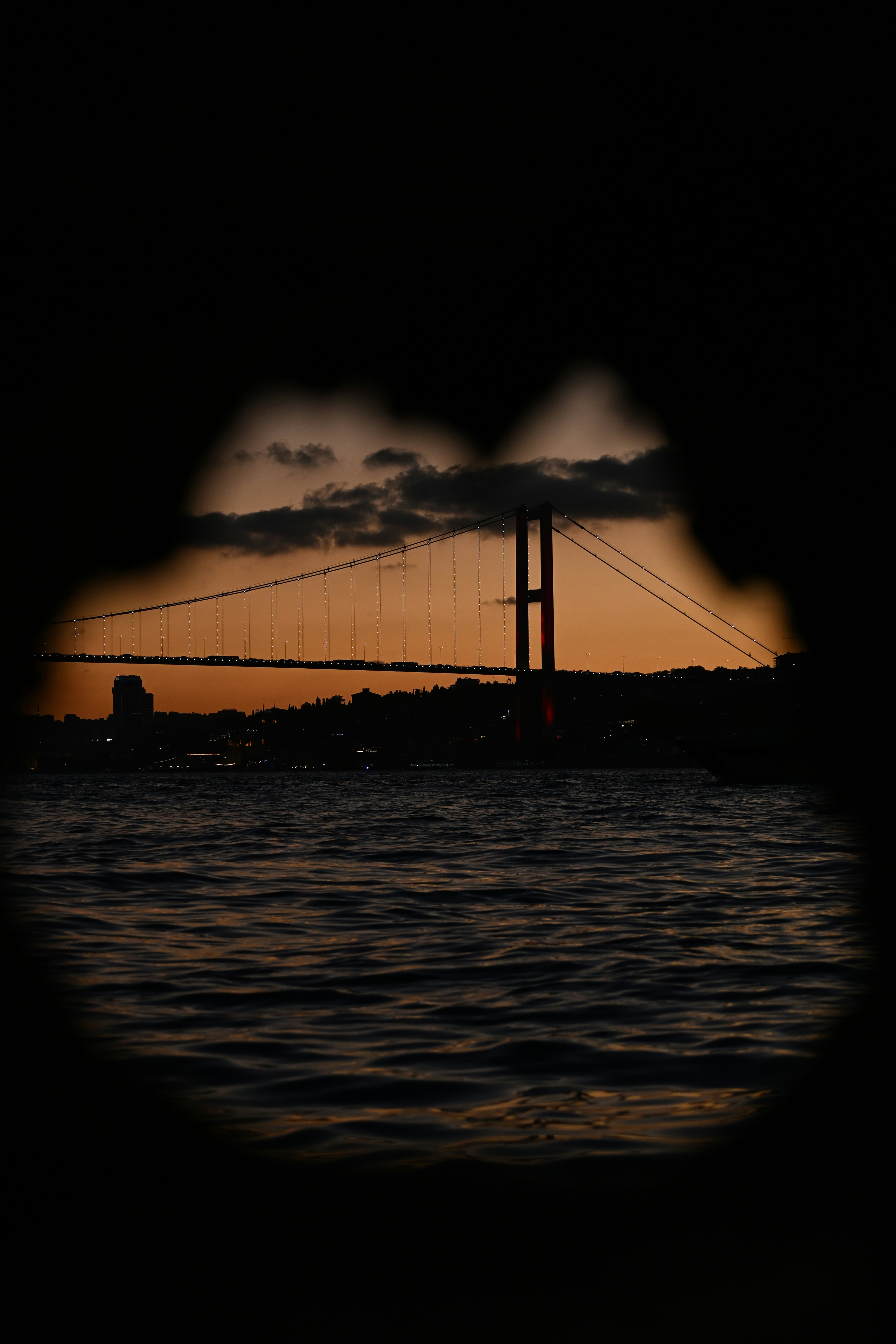 The Bosphorus Bridge silhouetted against a warm orange sky above dark water
