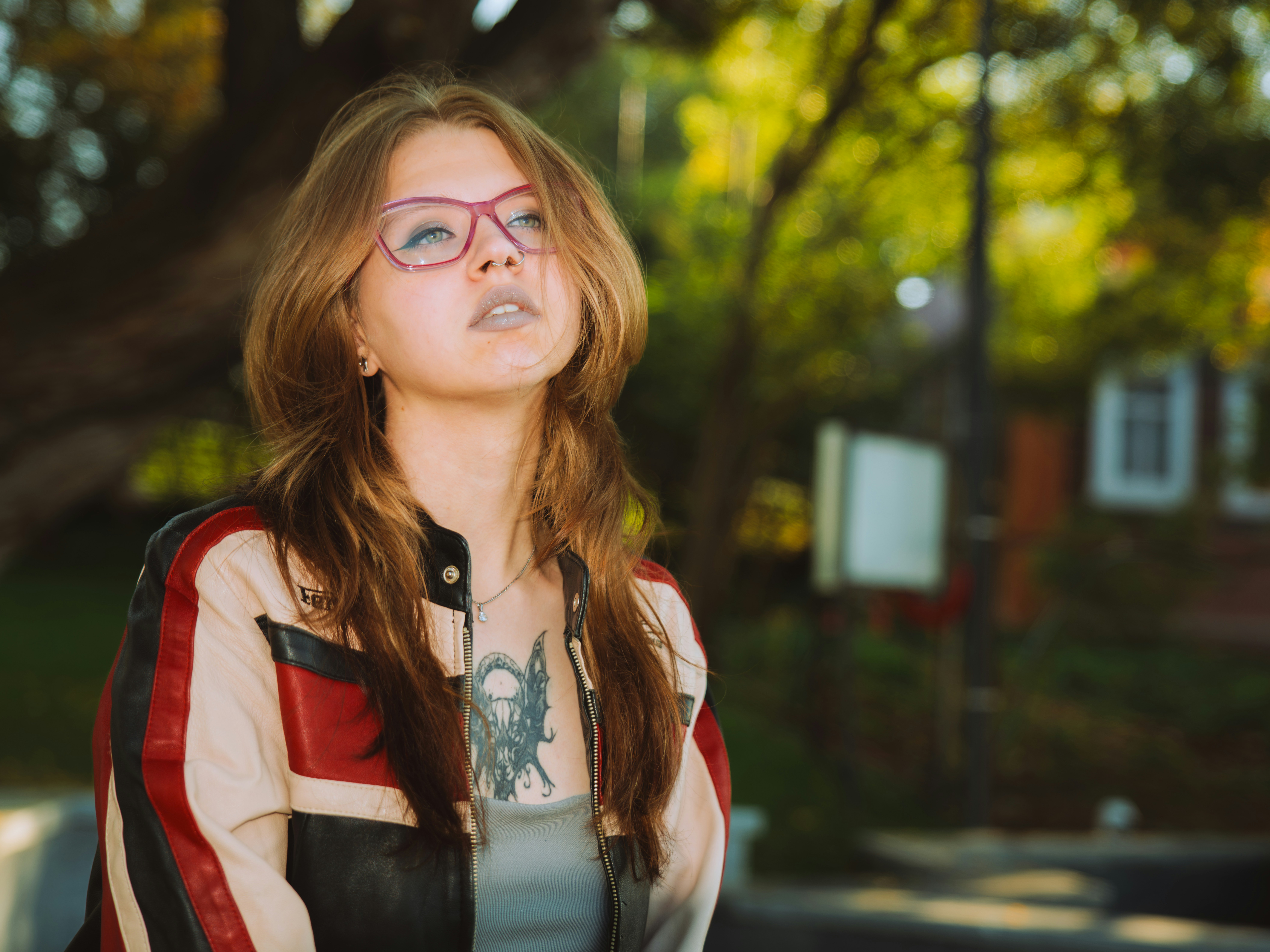 A woman with long brown hair wearing pink glasses and a leather jacket
