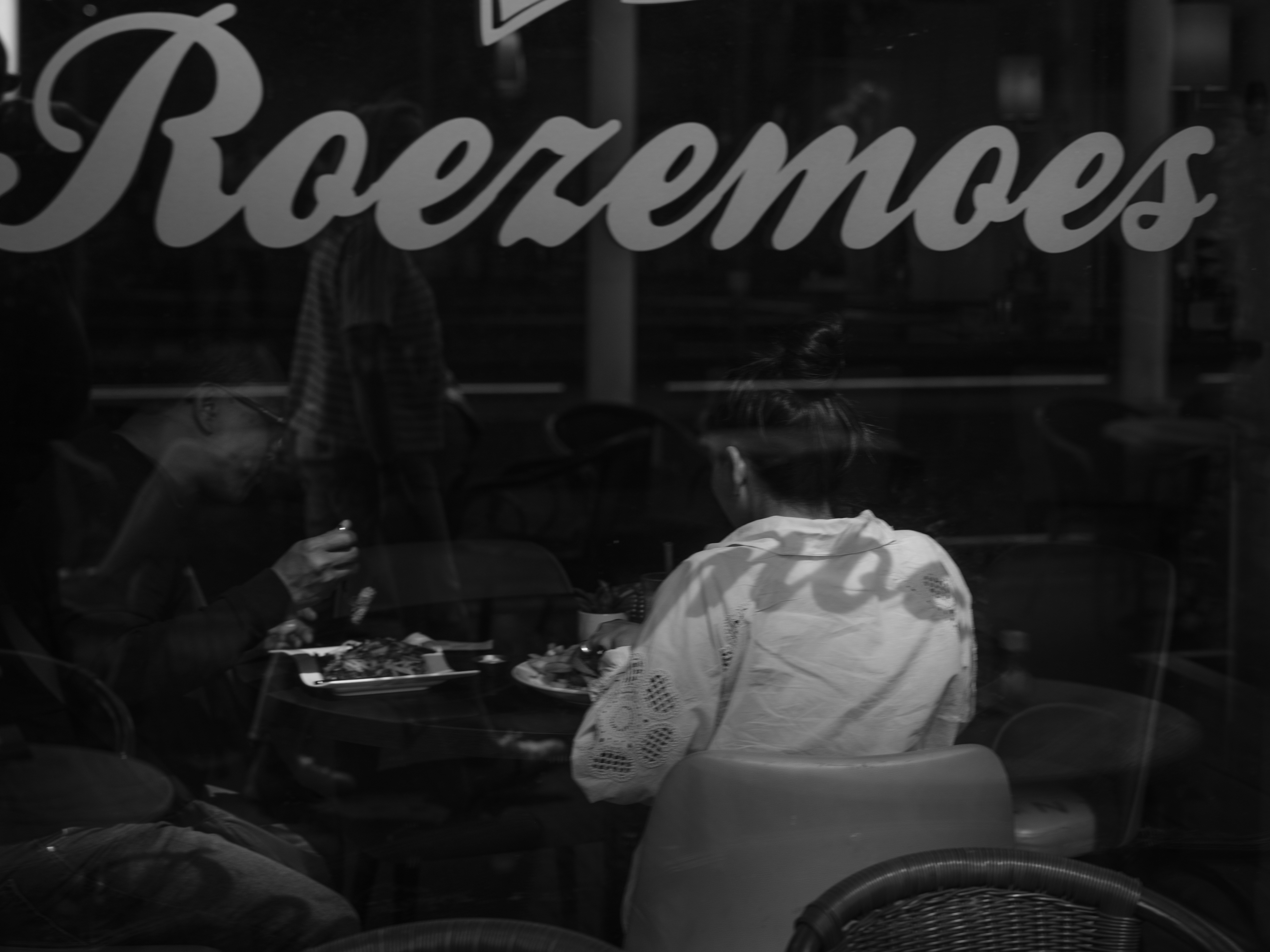 Two people eating at a table behind a window with the text Roeremoes