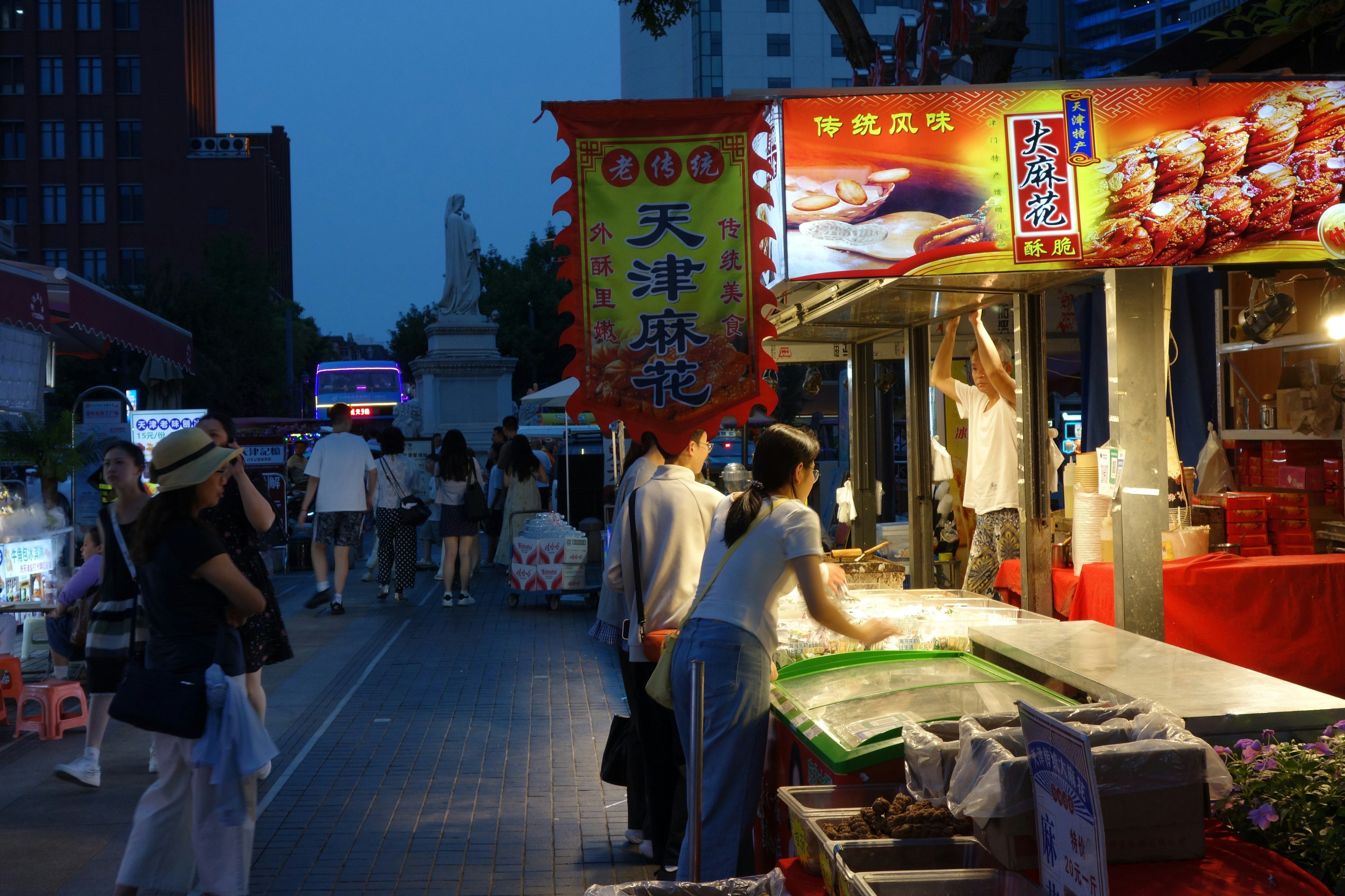 People walking along a street market at night with a food stall