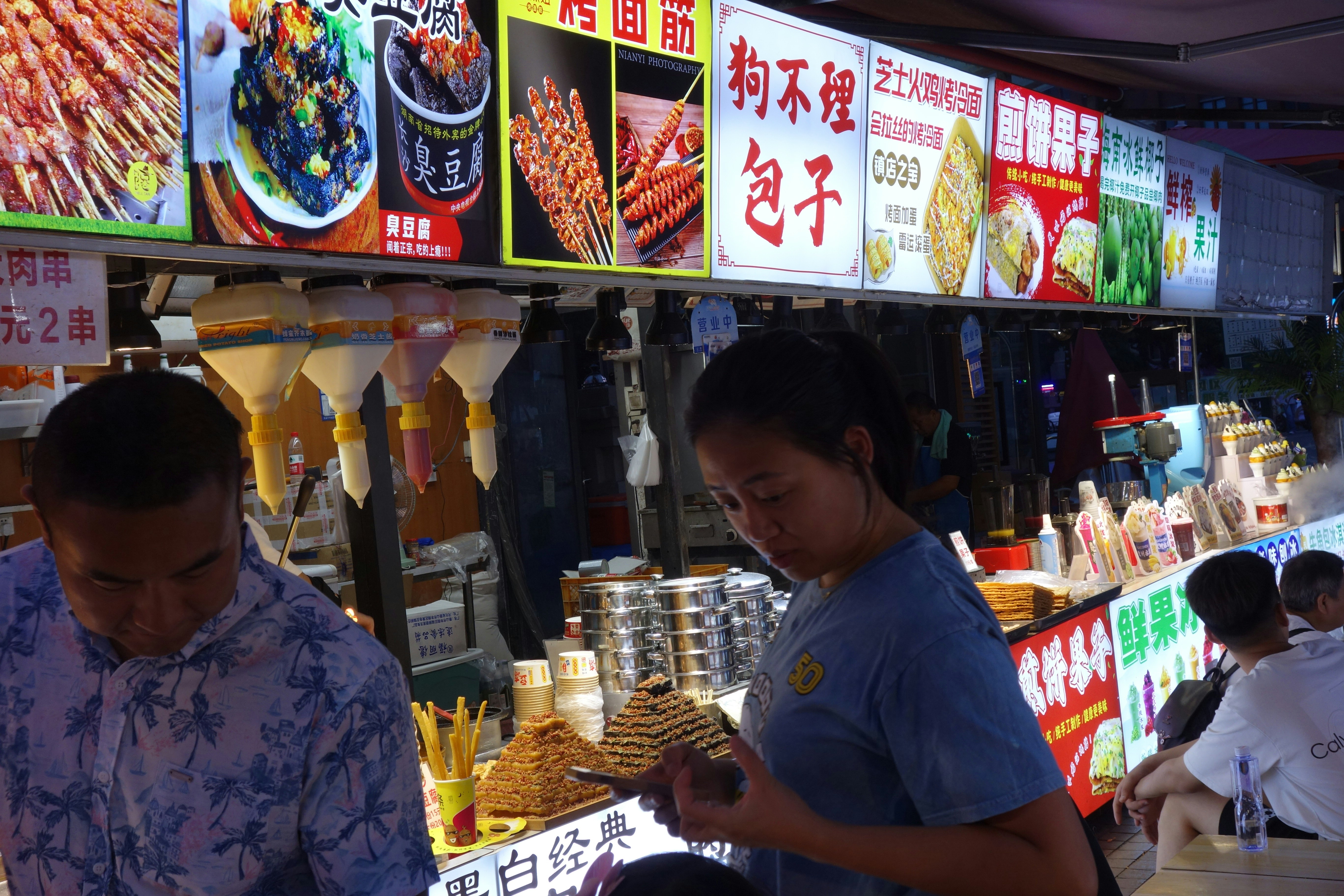 A woman looking at her phone at a street food stall with menu signs