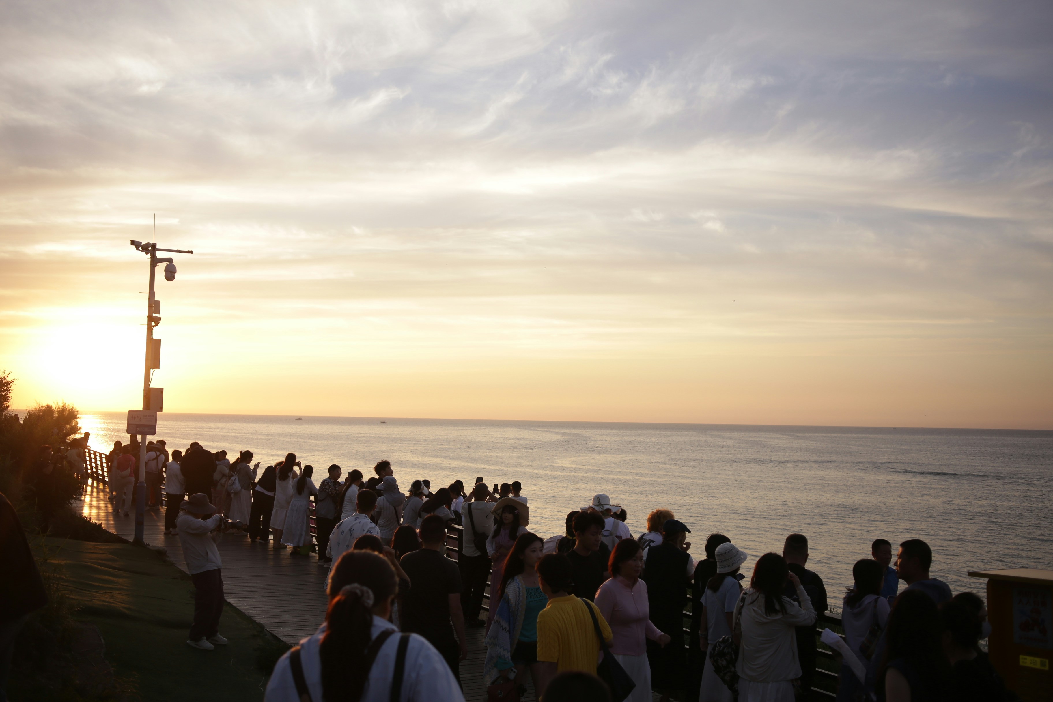 A group of people on a wooden boardwalk overlooking the ocean at golden hour