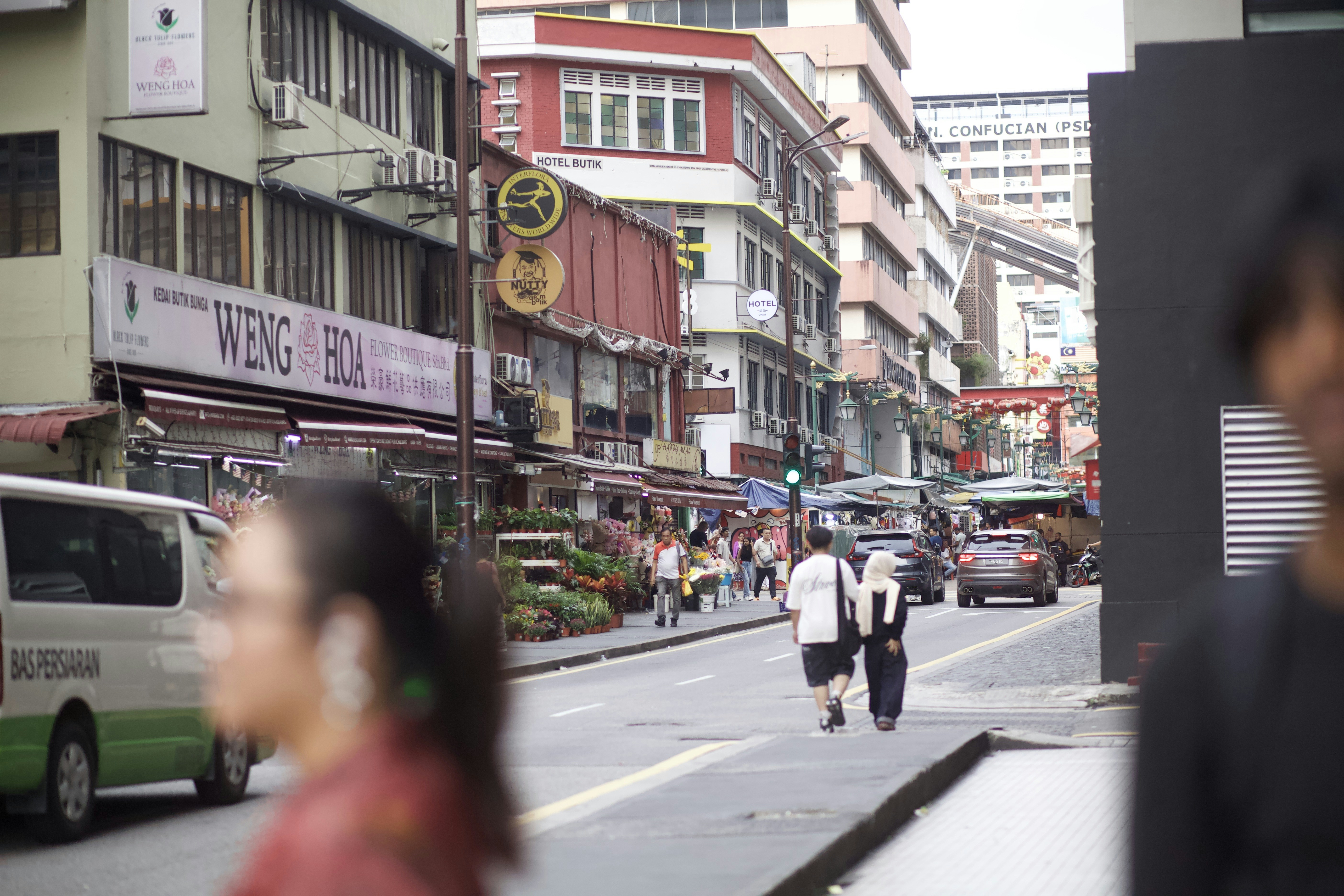 People walking along a street lined with flower shops and multi-story buildings