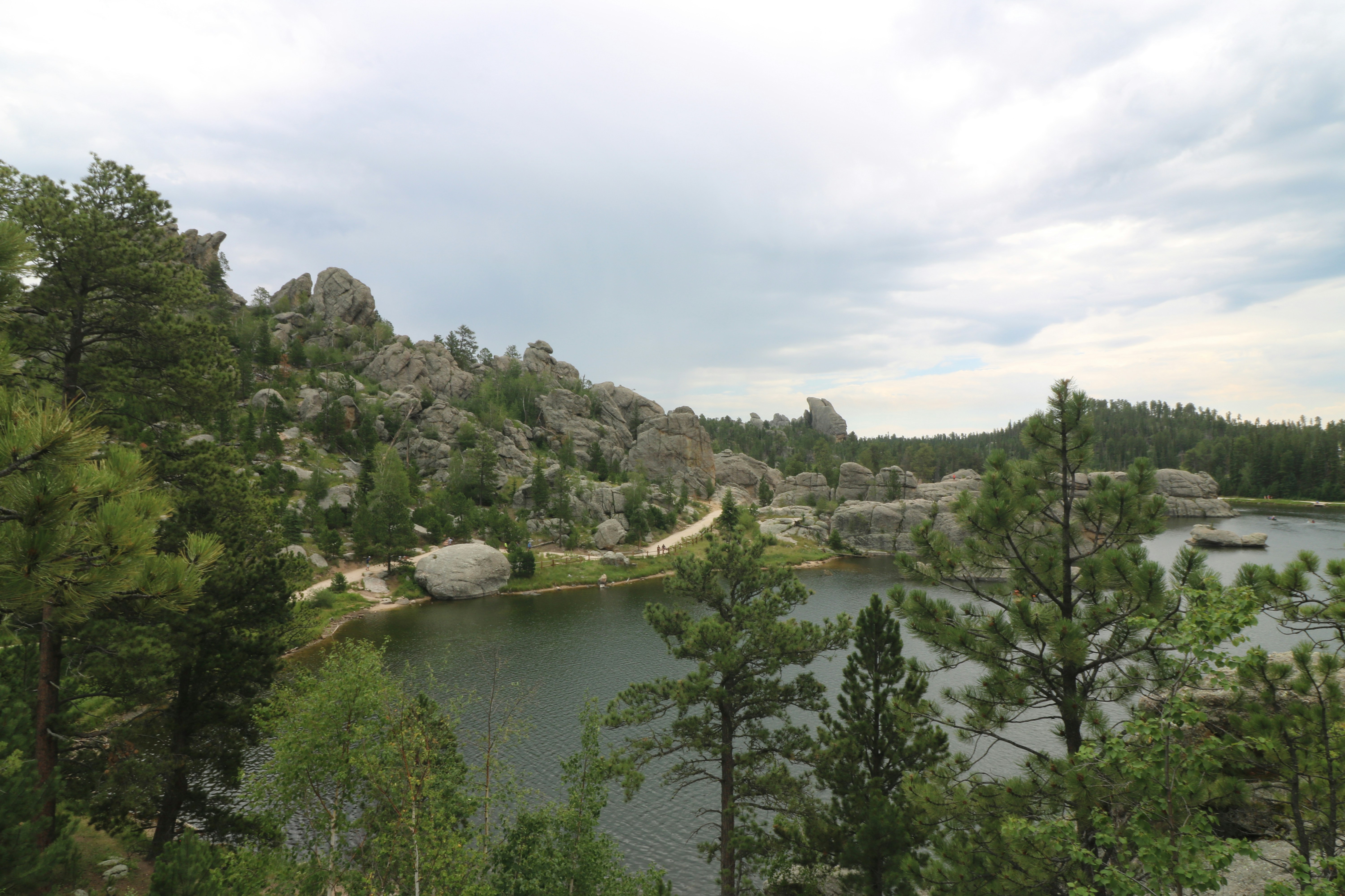 A lake surrounded by pine trees and large granite rock formations under cloudy skies