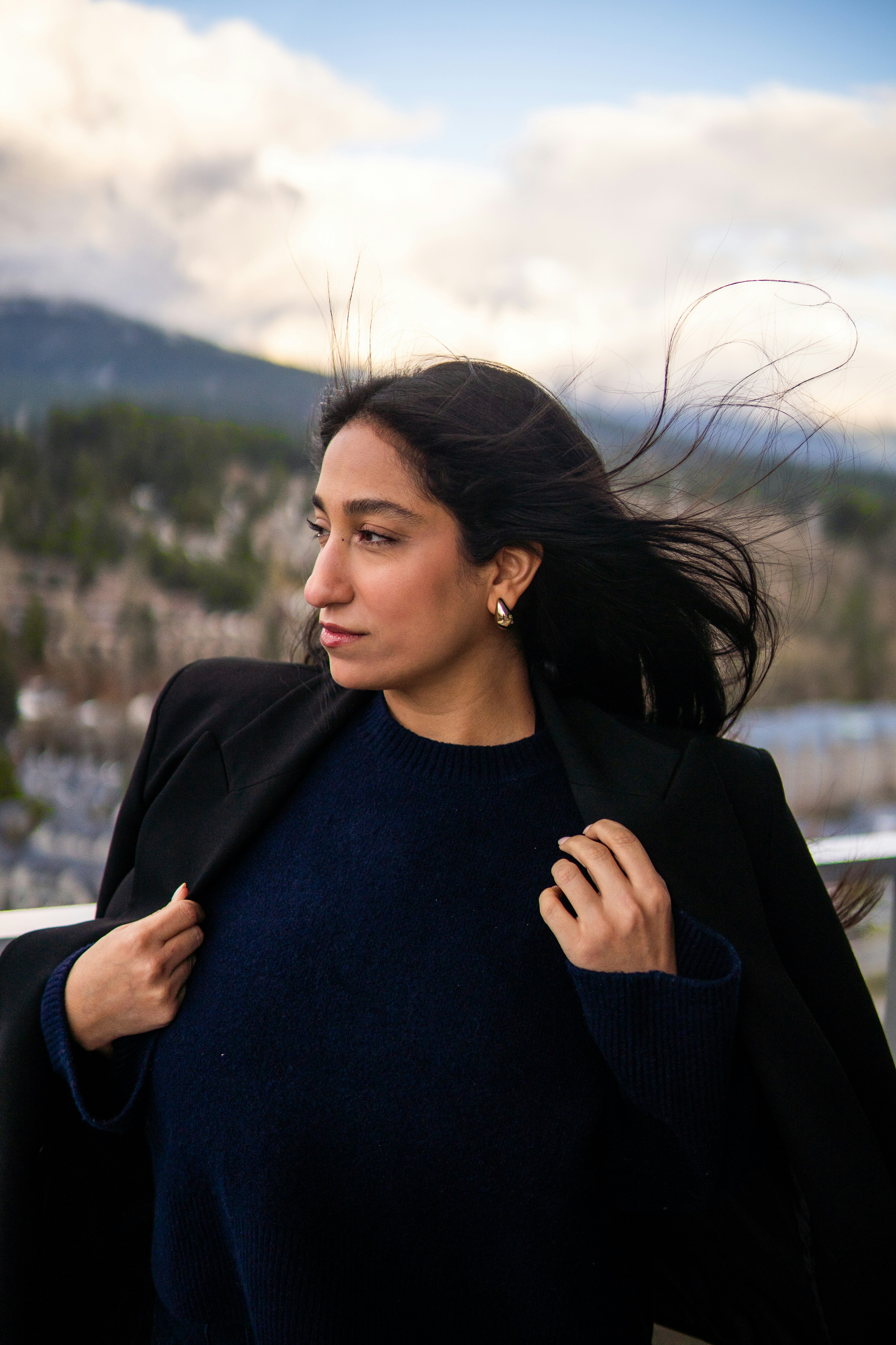 Eine Frau im dunklen Pullover und Blazer mit vom Wind verwehtem Haar draußen