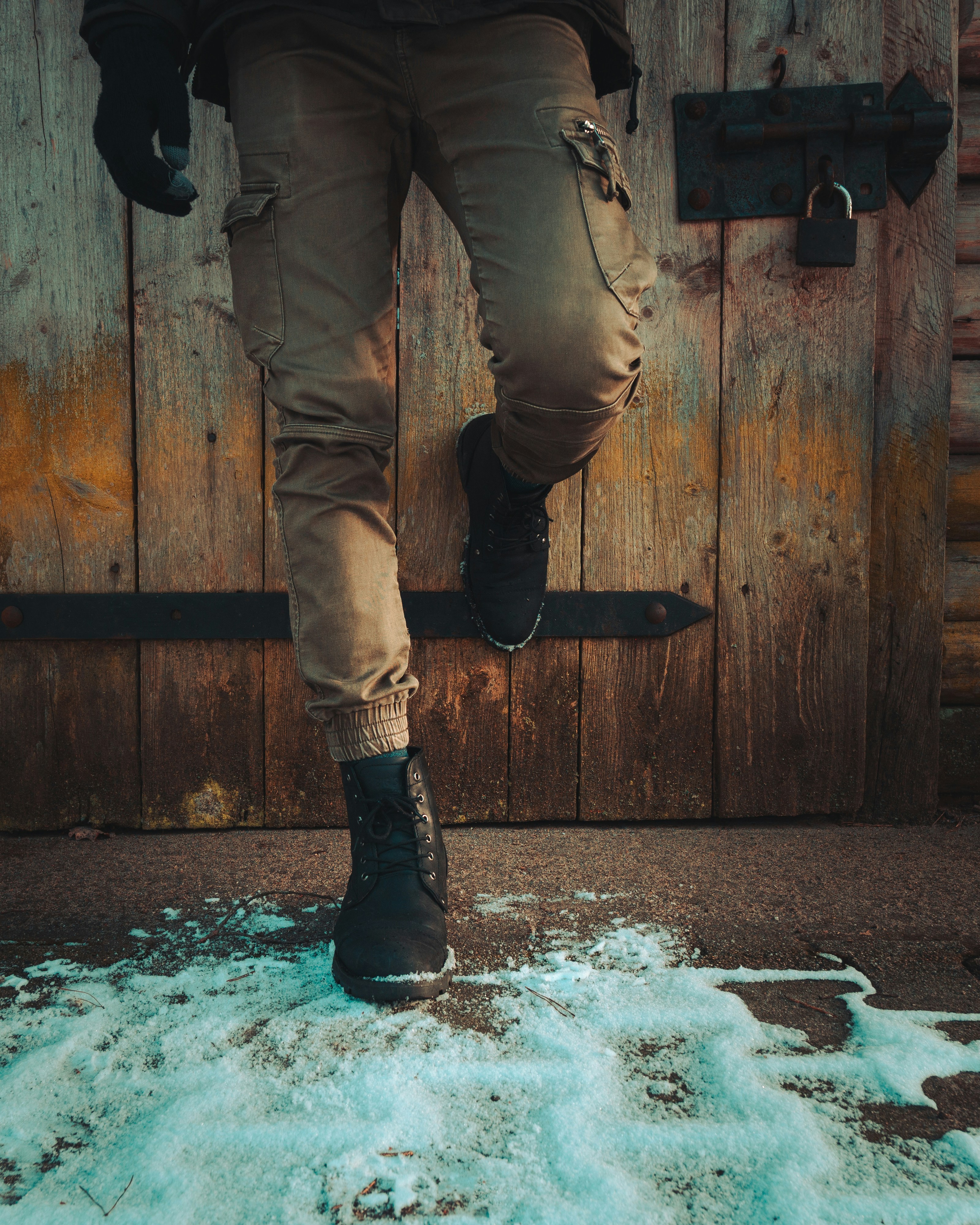 A person in olive cargo pants and black boots against a rustic wooden door