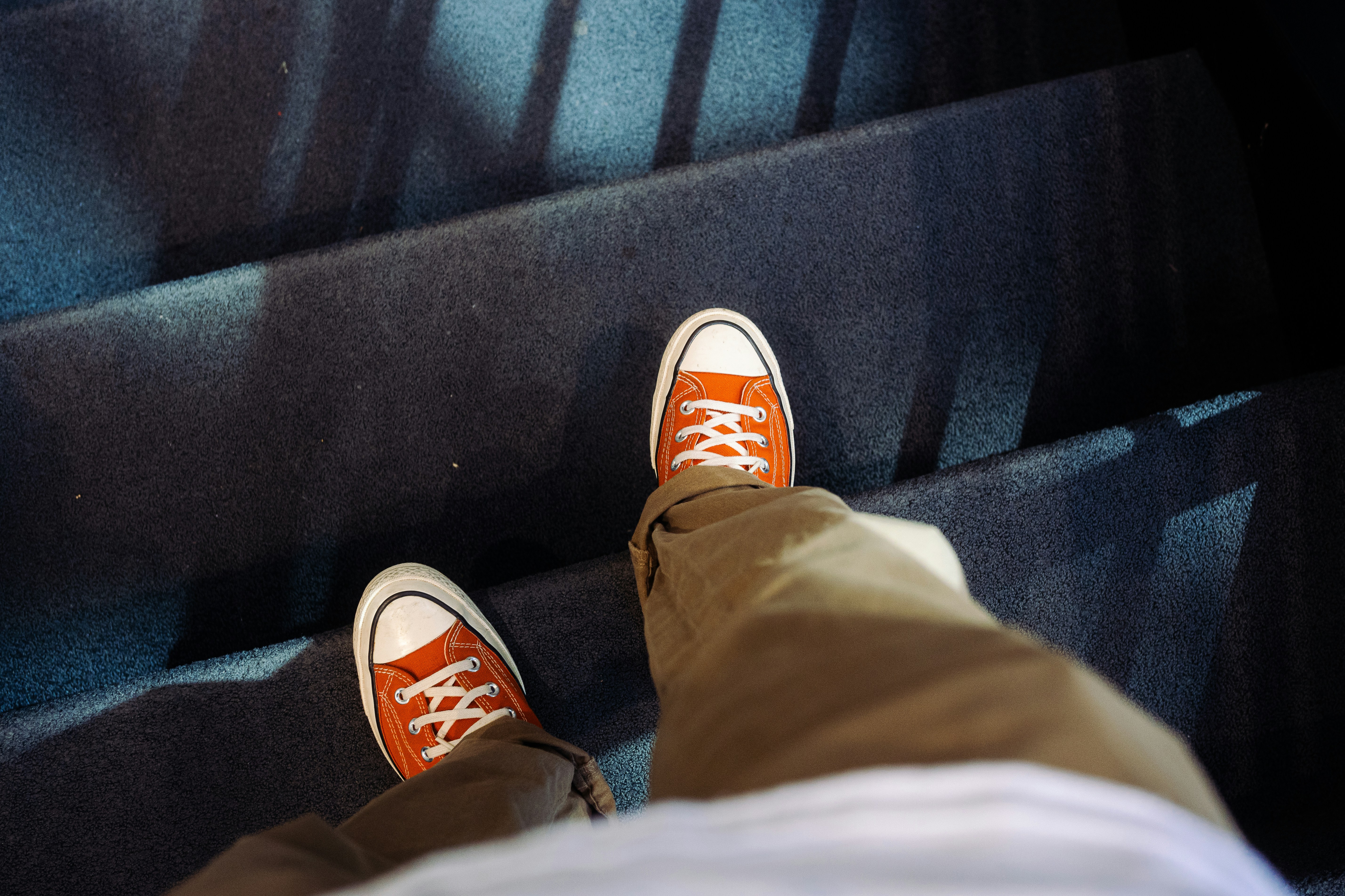 Eine Person, die orangefarbene Turnschuhe und khakifarbene Hosen trägt, geht die mit Teppich ausgelegten Treppen hinunter