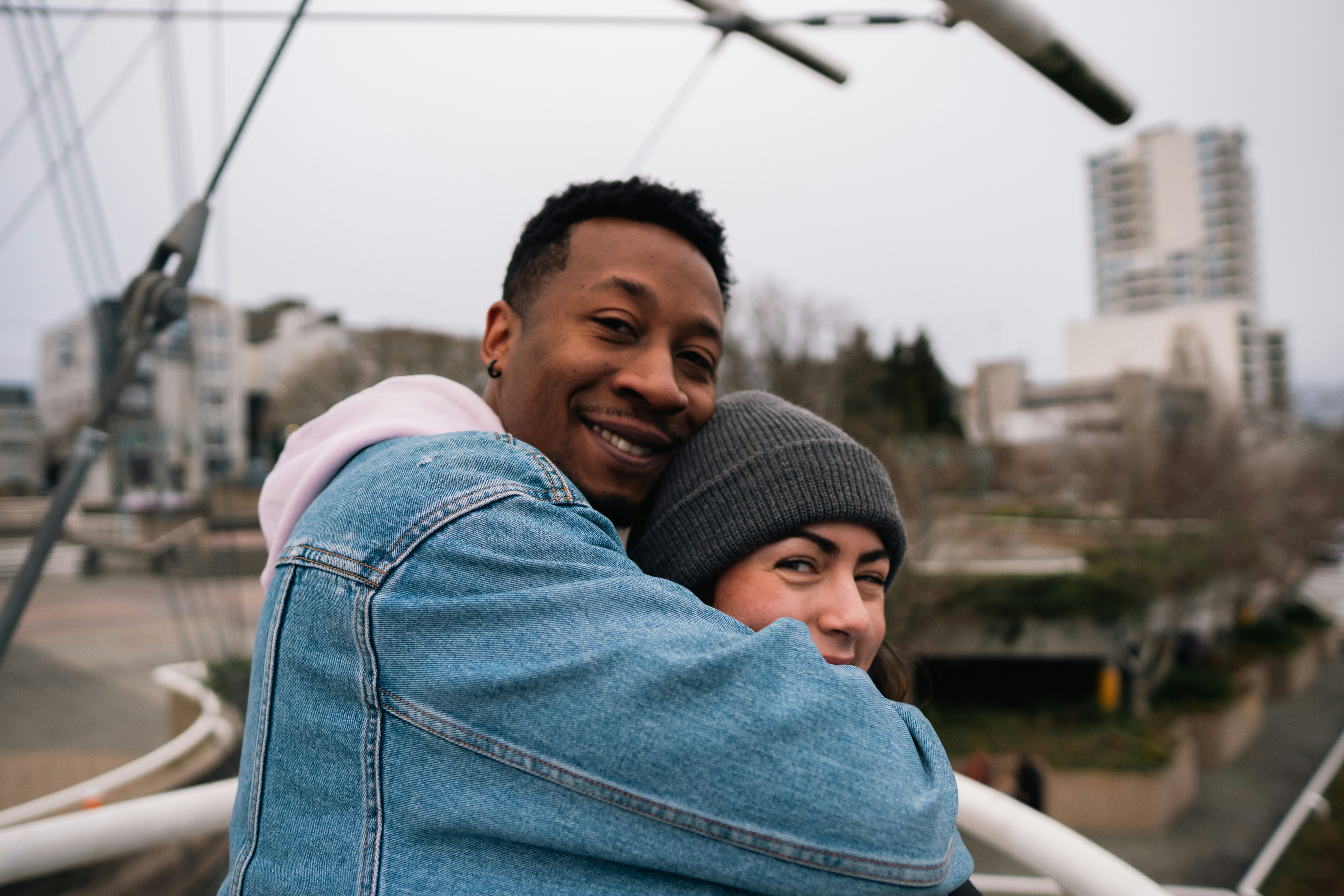 A man in a denim jacket hugging a woman in a grey beanie