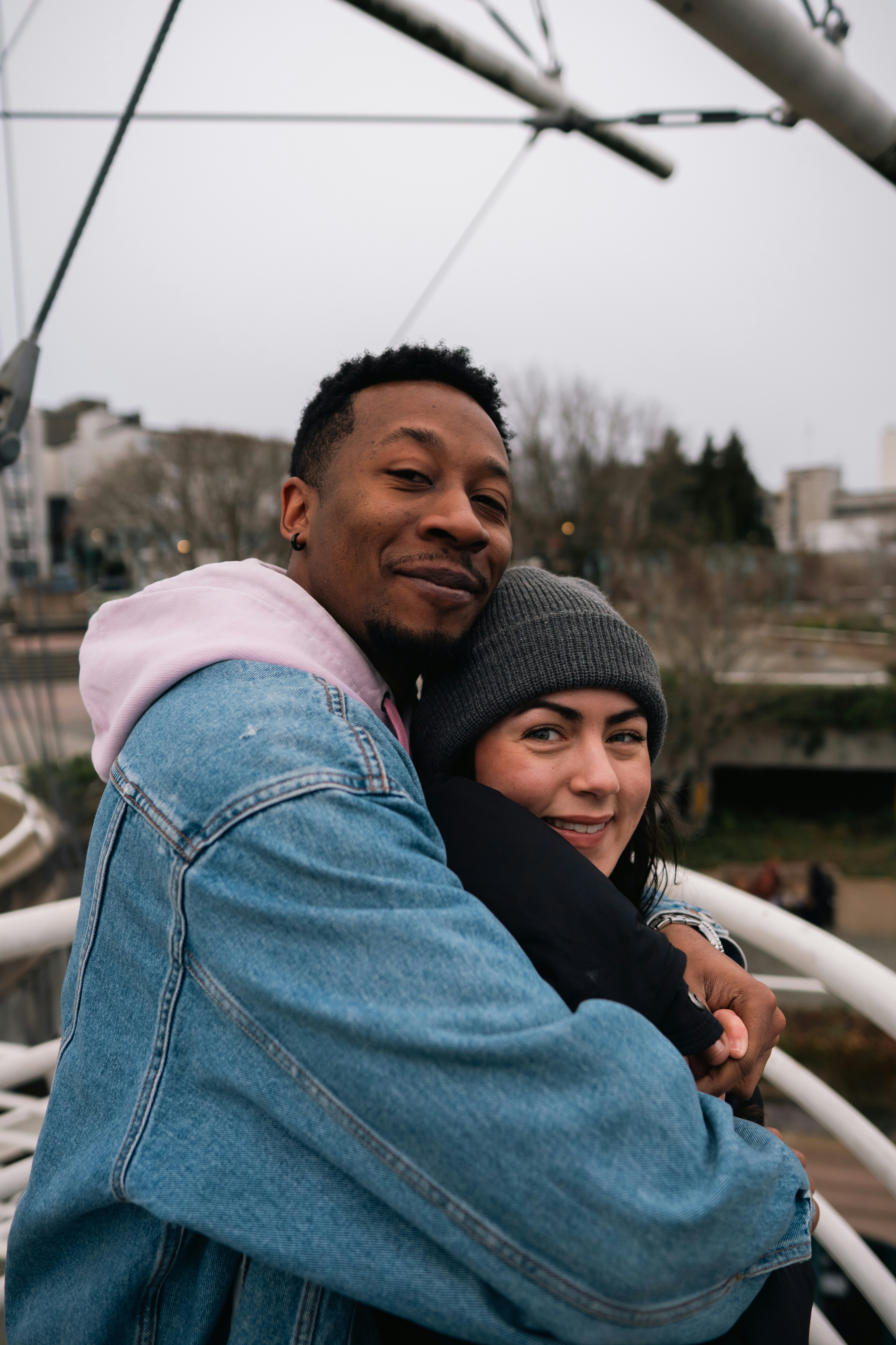 A man in a denim jacket hugging a woman in a grey beanie