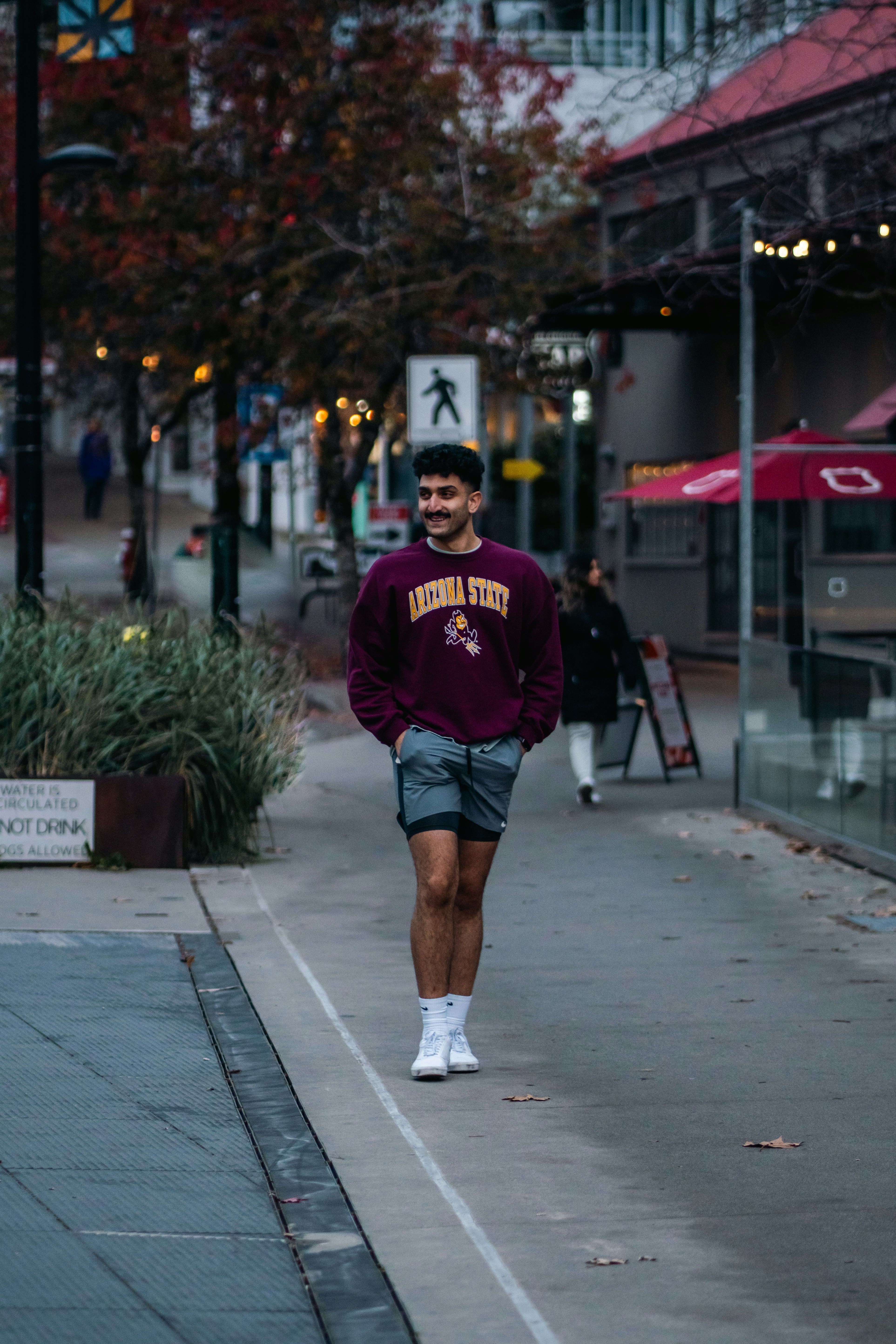 A man in a maroon Arizona State sweatshirt walking along a paved city path