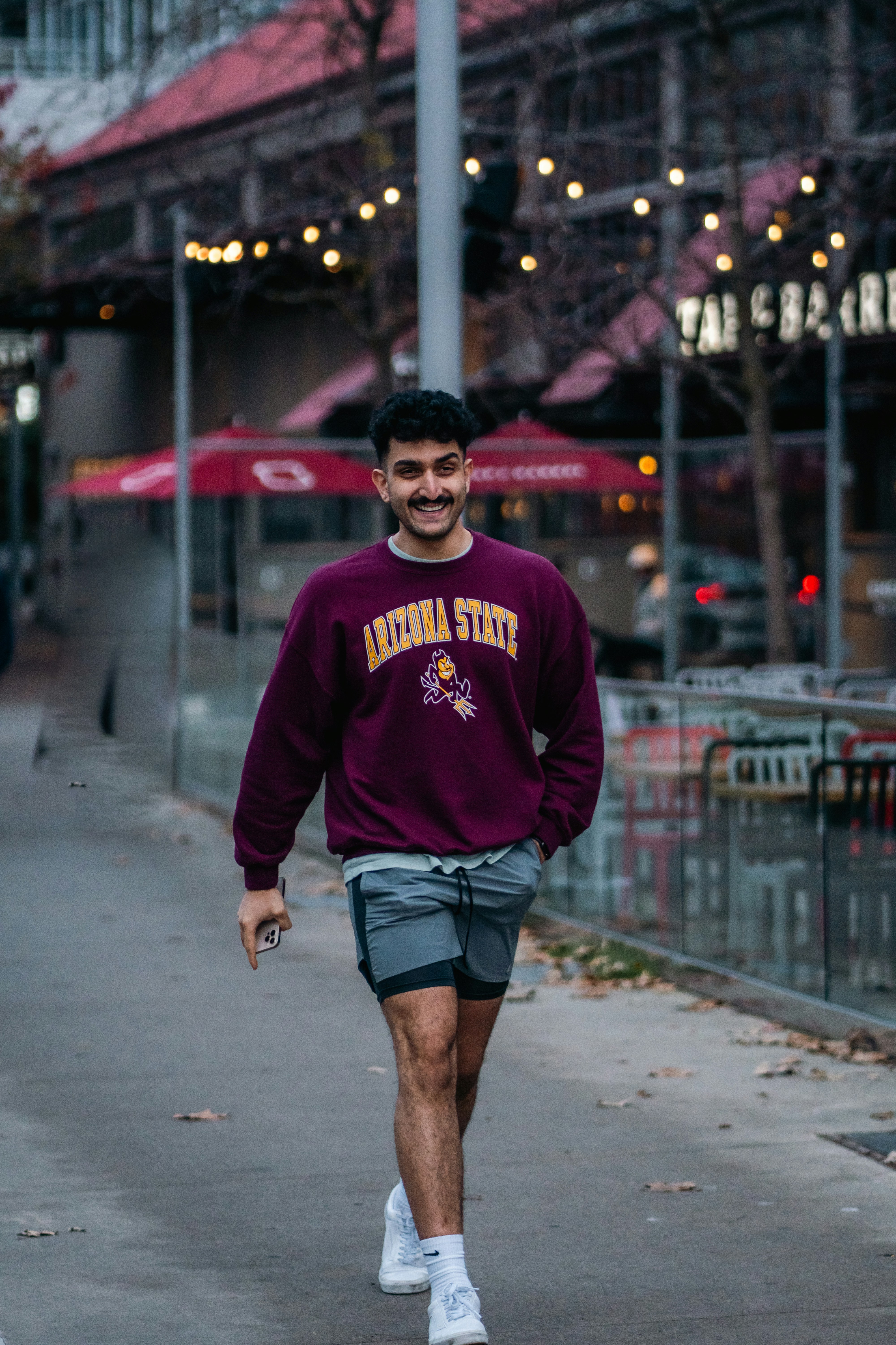 A smiling man in a maroon Arizona State sweatshirt walking on a sidewalk